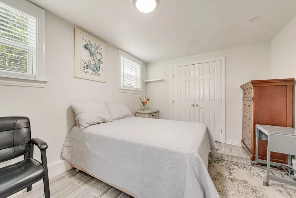 Neutral-toned interior featuring dual windows with horizontal blinds, wood-finish tile flooring, and a double-door closet with polished nickel hardware