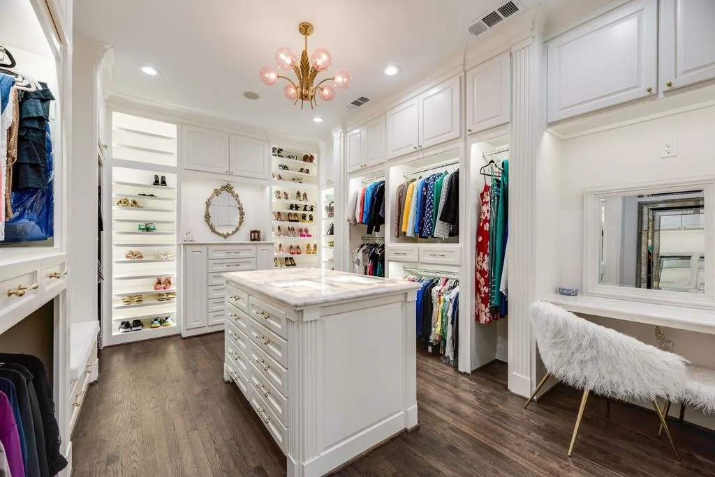 Custom built-in cabinetry featuring extensive shelving, central island with stone-finish countertop, recessed lighting, brass-finish chandelier, and wood-finish flooring