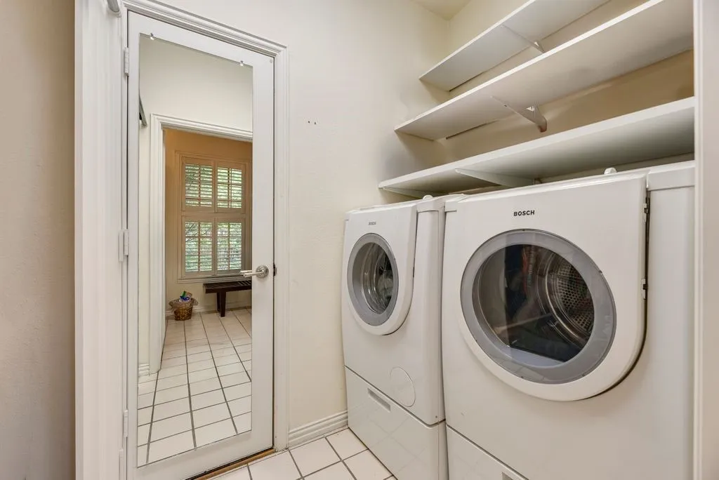 Laundry room featuring Bosch white front-load washer and dryer, white ceramic tile flooring, and overhead built-in shelving
