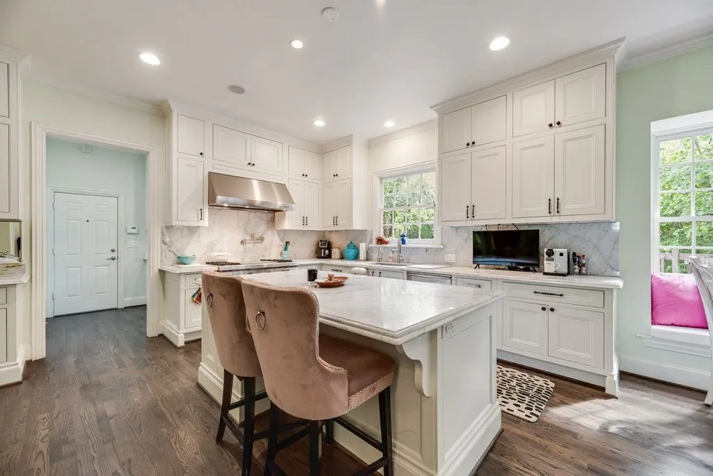 Kitchen featuring white shaker cabinetry, stone-surface countertops, full-height stone backsplash, stainless steel range hood, and wood-finish flooring