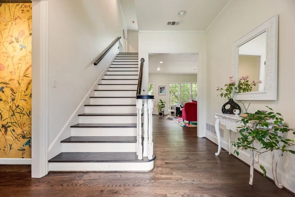 Foyer featuring wood-finish flooring, a staircase with dark-stained treads, white risers, and a decorative handrail, and an accent wall with floral wallcovering