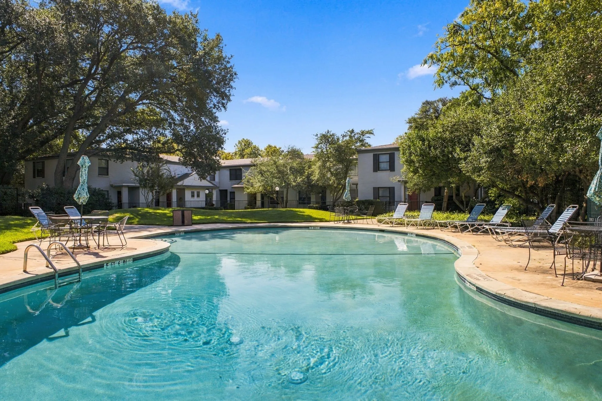Swimming pool with concrete decking, surrounded by mature trees and landscaped grass areas