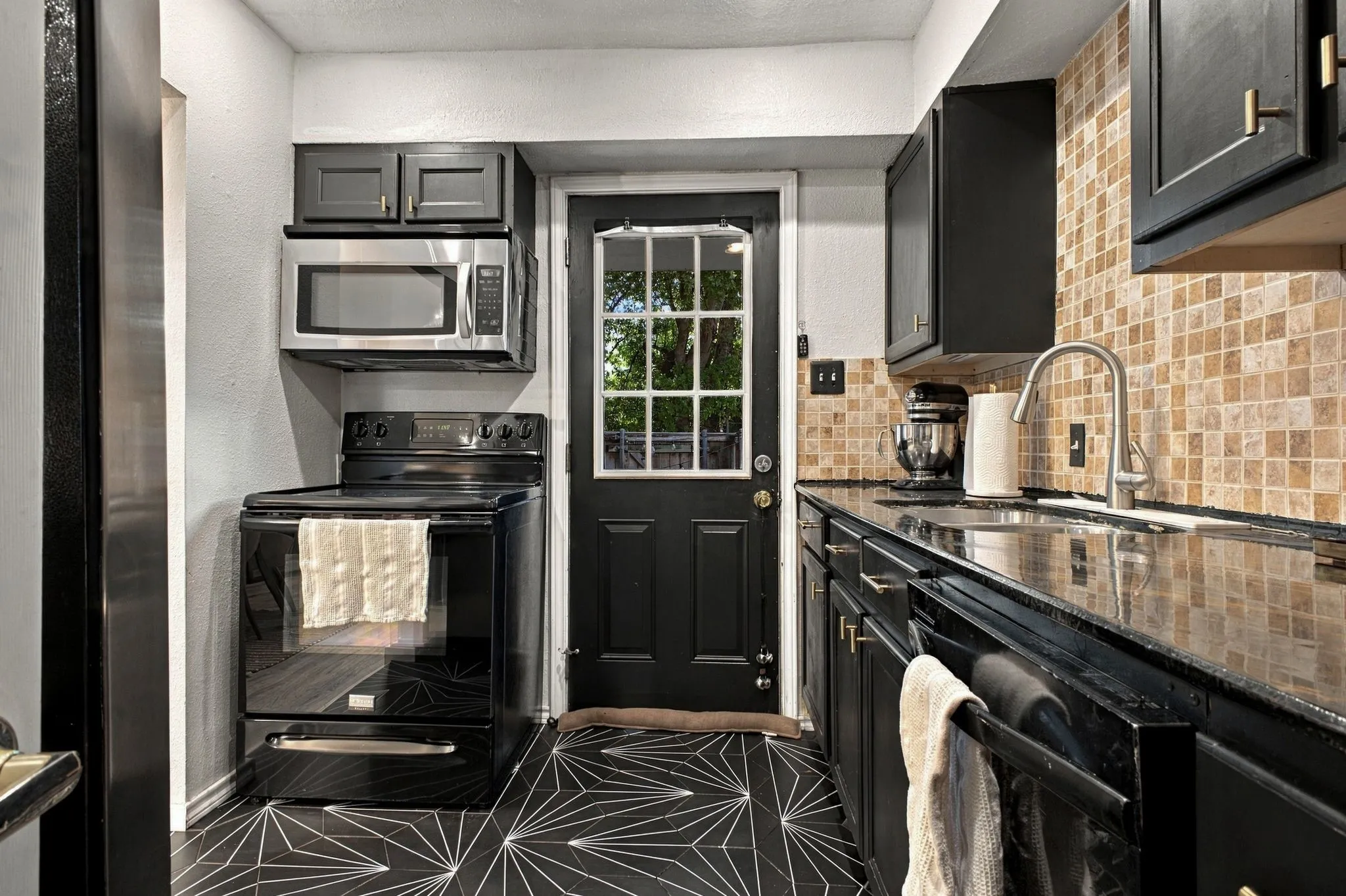 Kitchen featuring dark cabinetry, polished stone countertops, mosaic tile backsplash, geometric patterned flooring, and a stainless steel appliance suite
