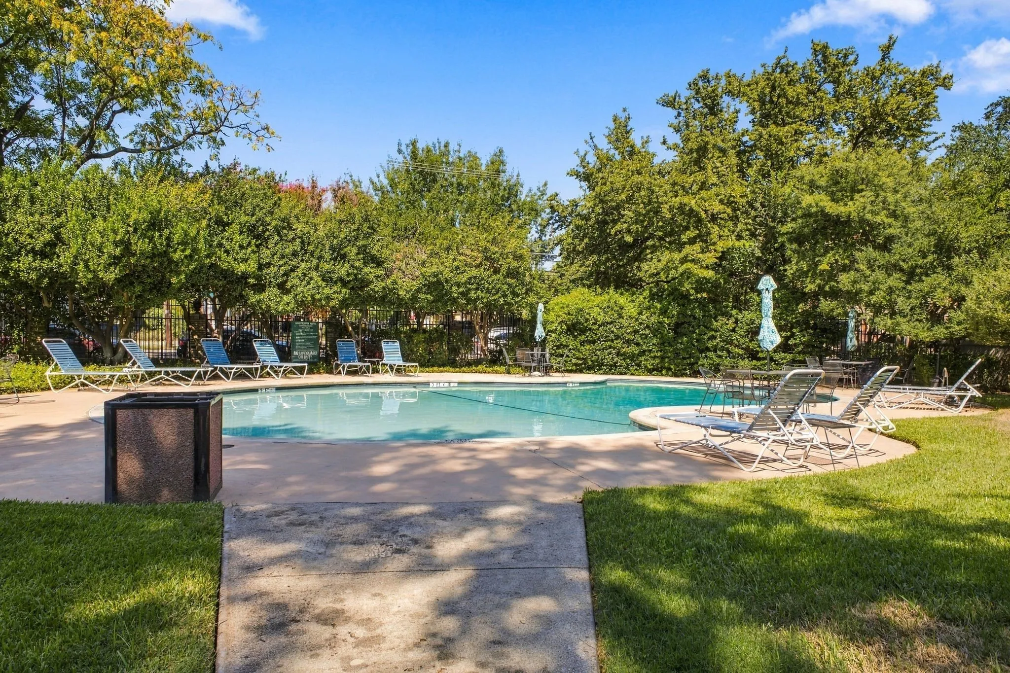 In-ground swimming pool featuring a concrete surround, surrounded by mature trees and landscaped grounds