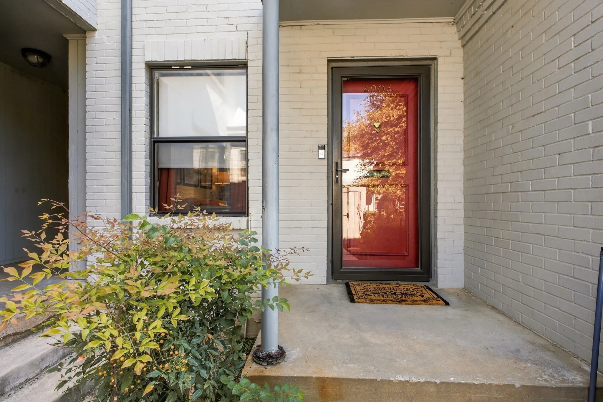 Painted white brick exterior featuring a red entry door, storm door, single-hung window, and a concrete porch