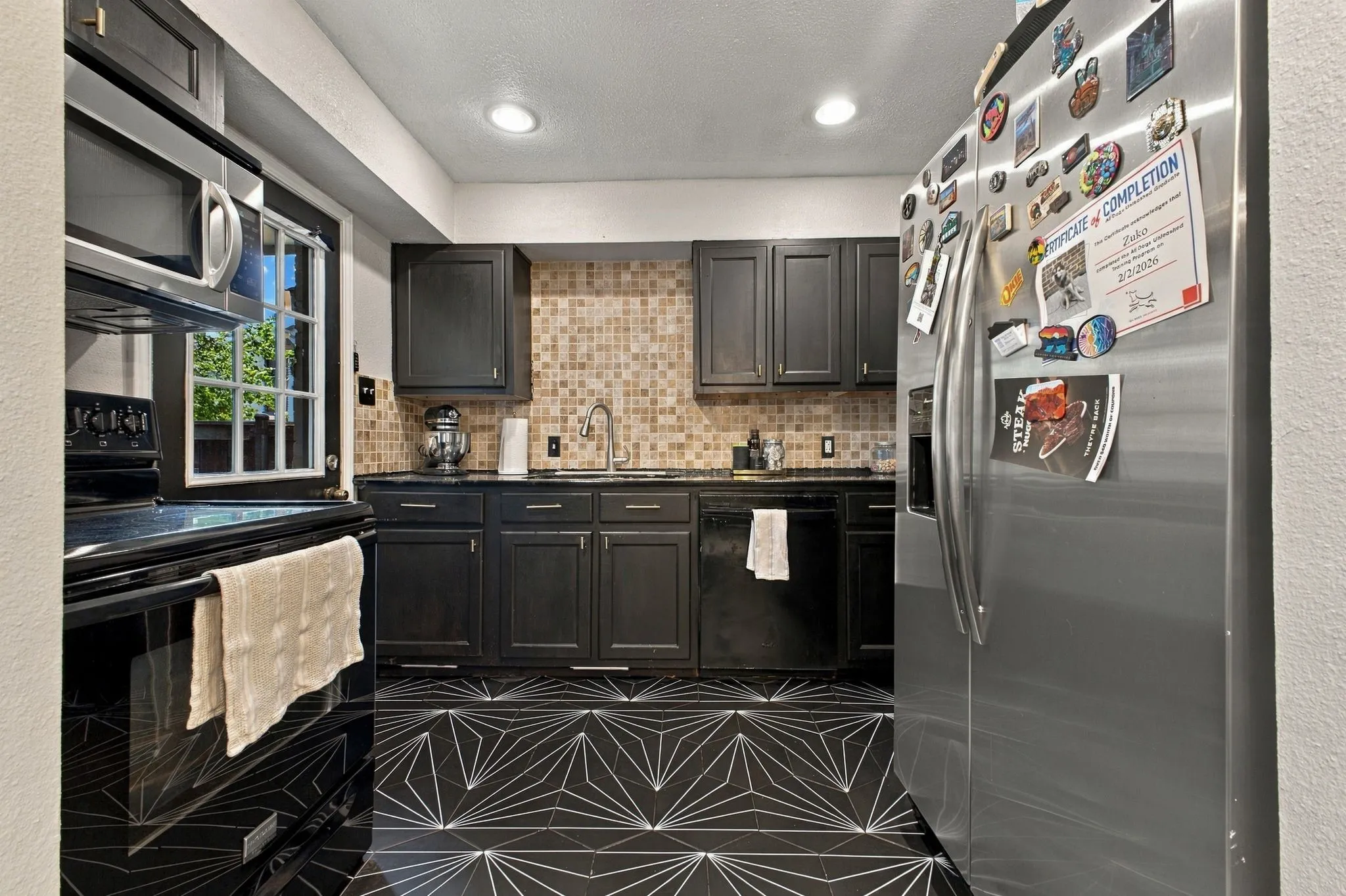 Kitchen featuring dark cabinetry, geometric-patterned tile flooring, stone-tiled backsplash, recessed lighting, and stainless steel appliances