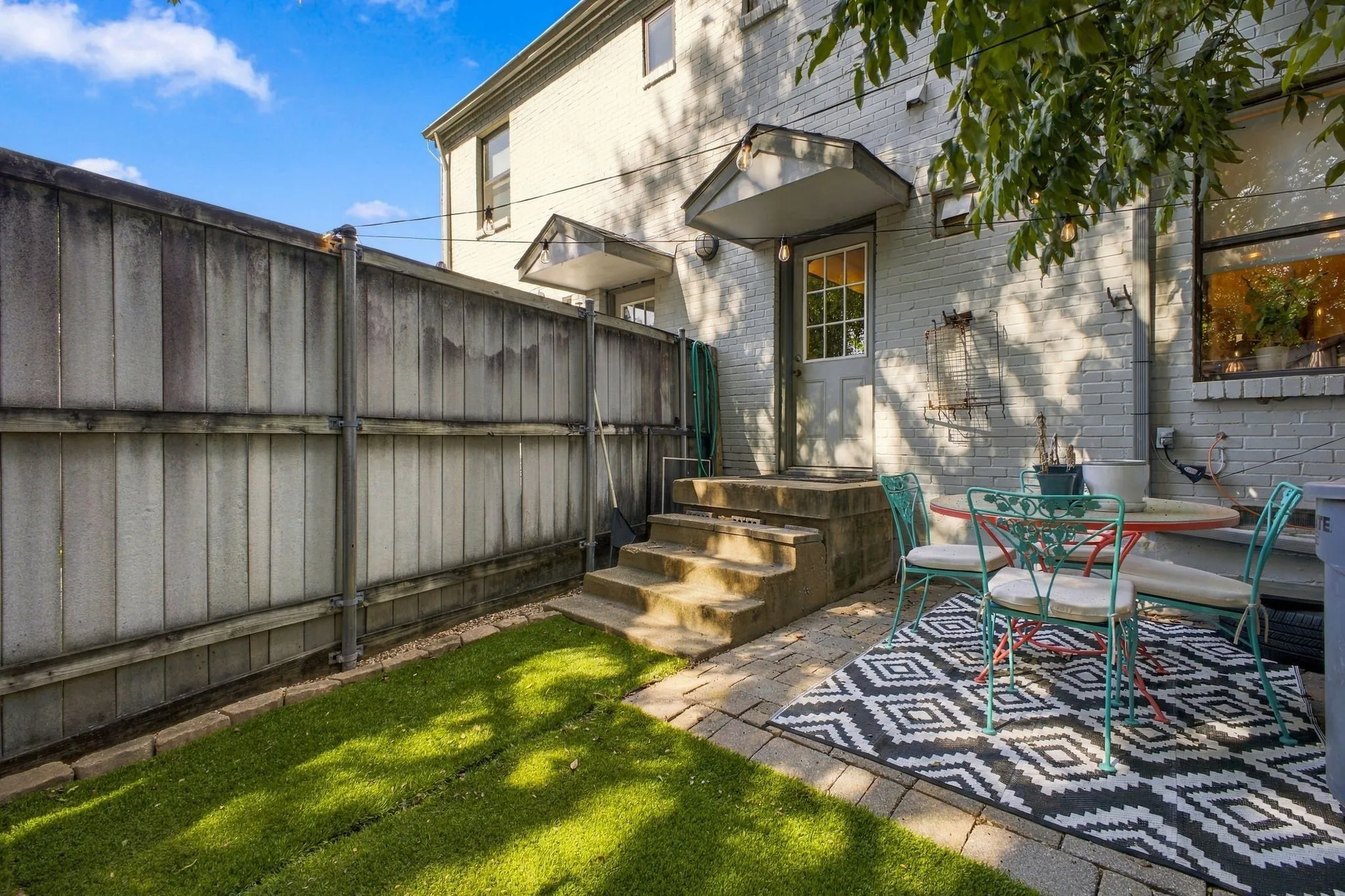 Fenced backyard featuring a paver patio, synthetic turf lawn, and a brick exterior with metal door awnings