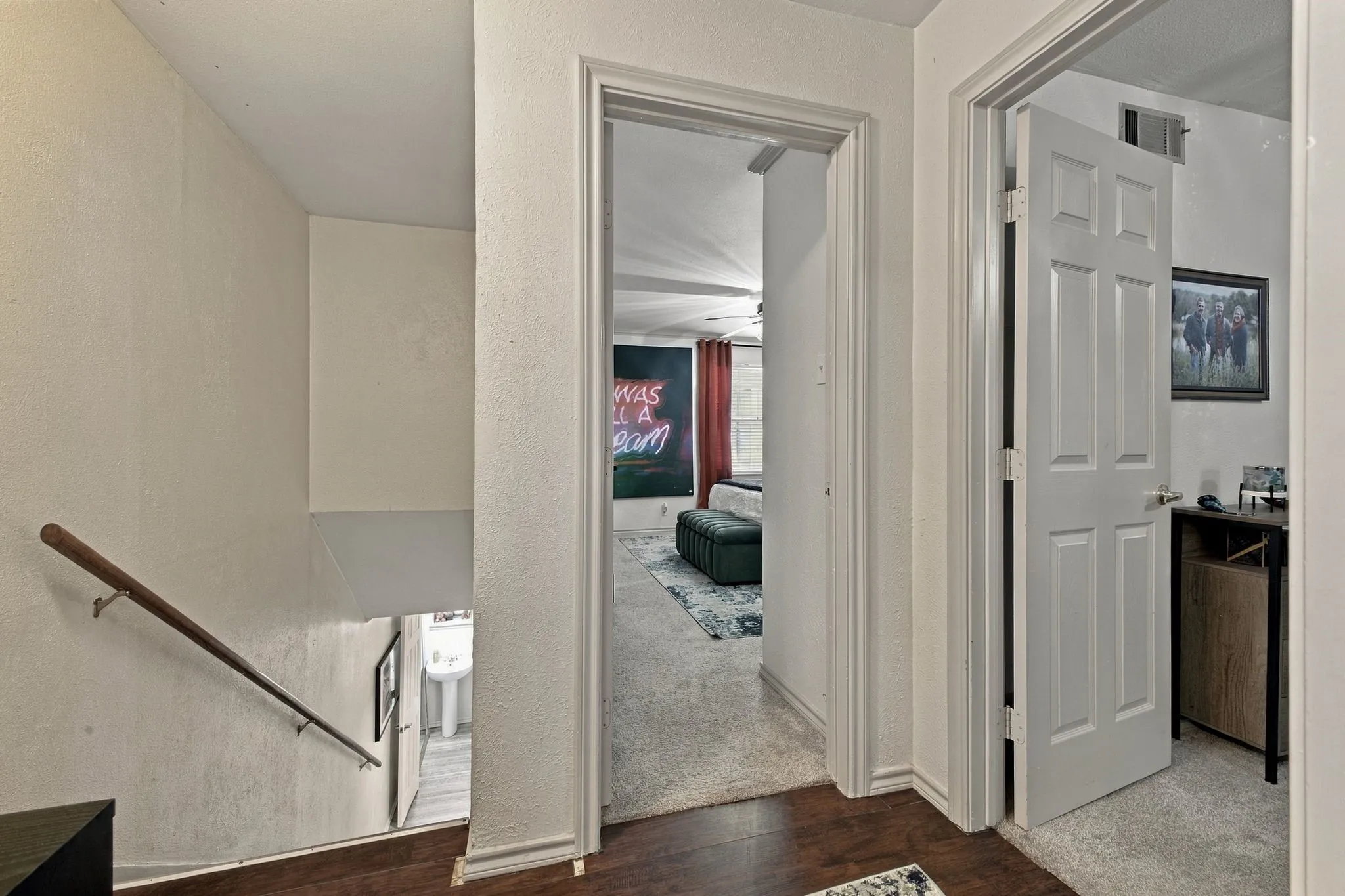 Interior hallway featuring wood-finish flooring, white paneled doors, and a staircase with a mounted metal handrail