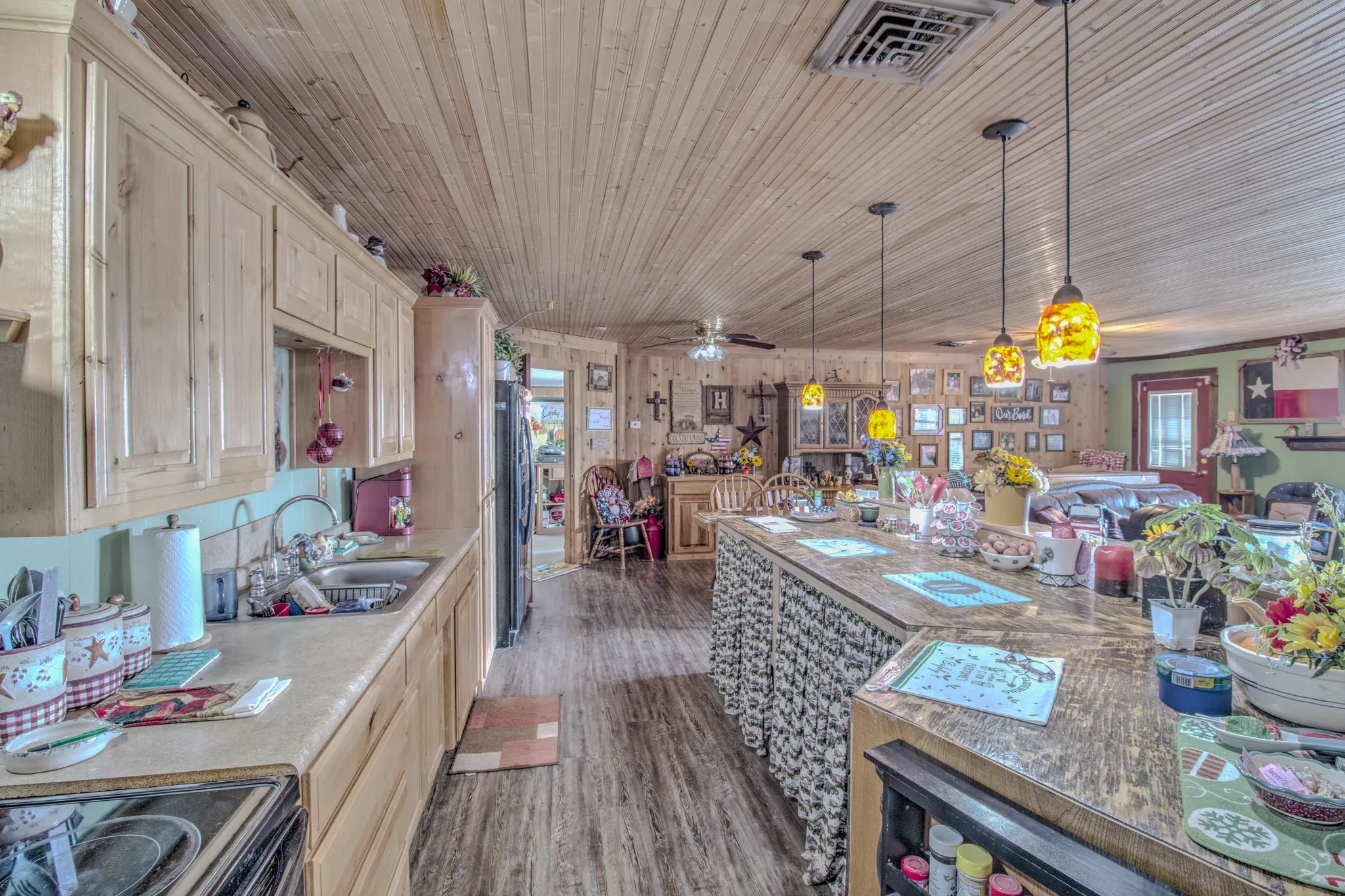 Kitchen featuring wood-paneled walls and ceilings, cabinetry with natural wood finish, a stone-patterned countertop, a central island, and three pendant light fixtures