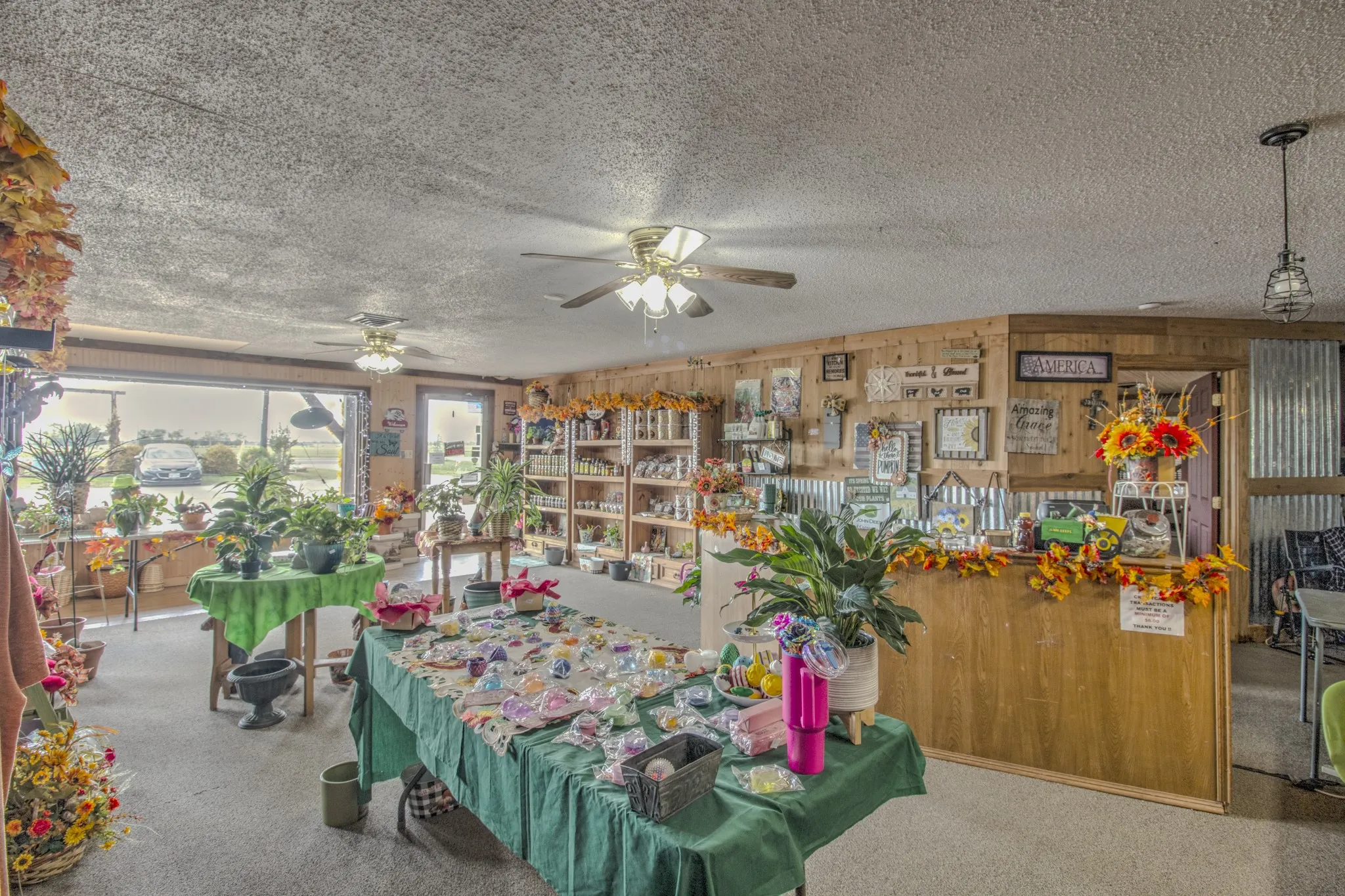 Open-concept commercial space featuring wood-paneled walls, corrugated metal wainscoting, dual ceiling fans, and a built-in transaction counter