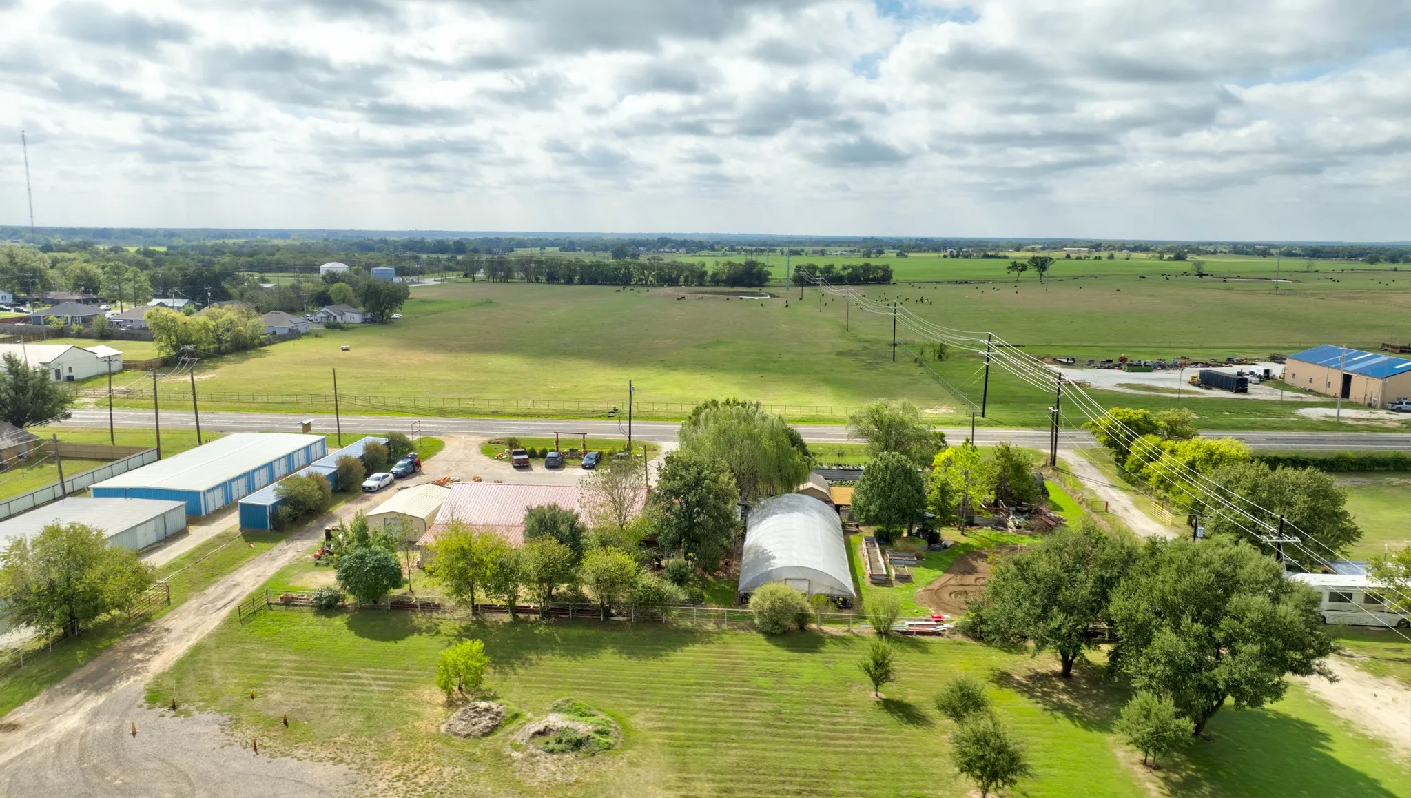 Expansive rural acreage featuring multiple outbuildings, metal-roof structures, a greenhouse, and open pasture land