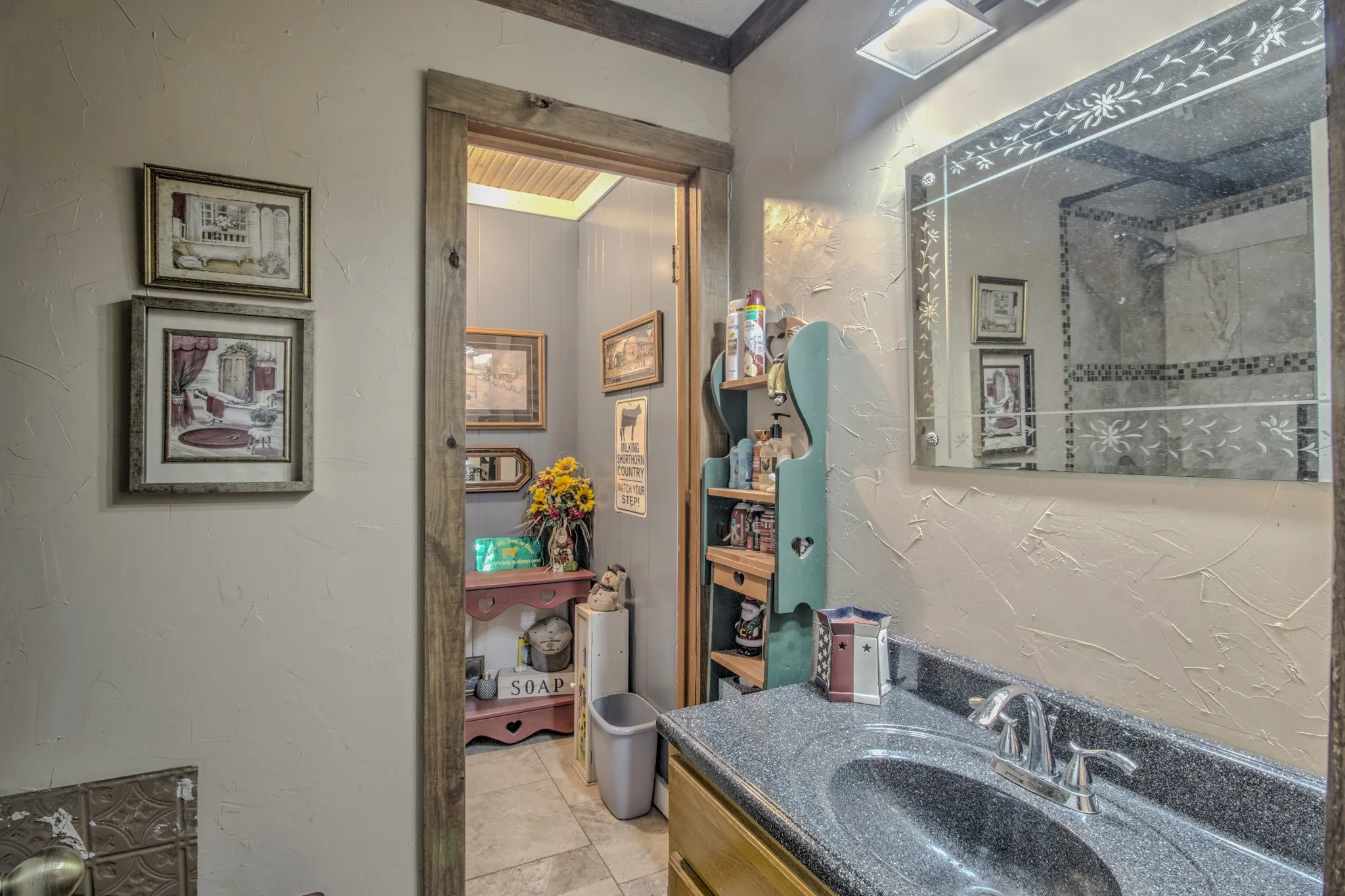 Bathroom featuring a vanity with a stone-composite countertop, integrated sink, and polished chrome faucet, paired with a decorative etched-glass wall mirror and wood-trimmed door frame
