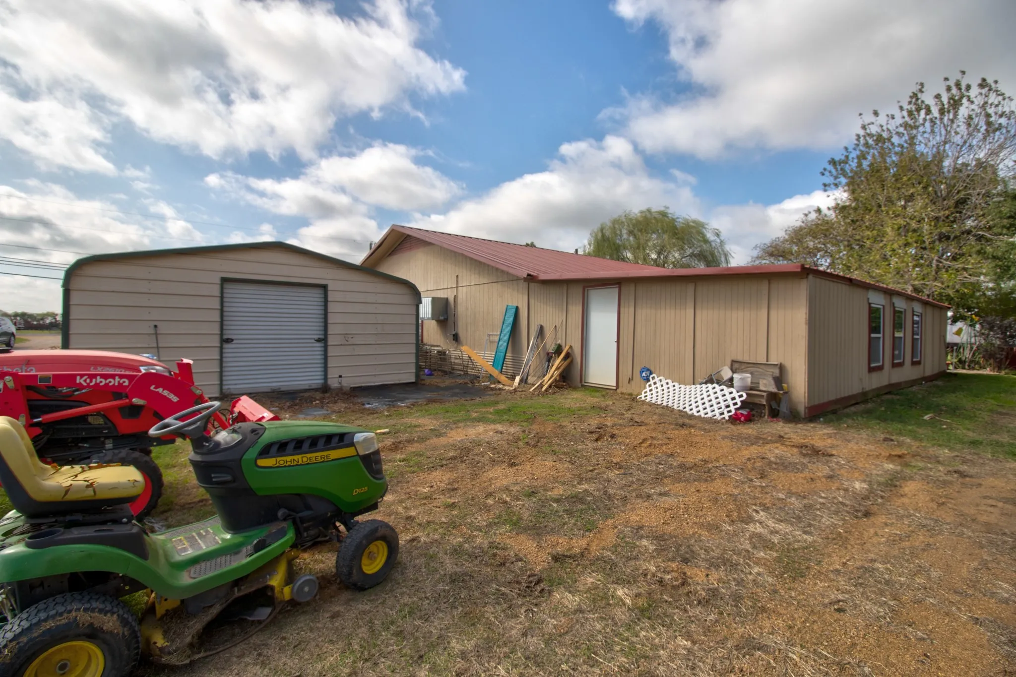 Single-story structure with metal siding and a red metal roof, accompanied by a detached metal-frame storage building
