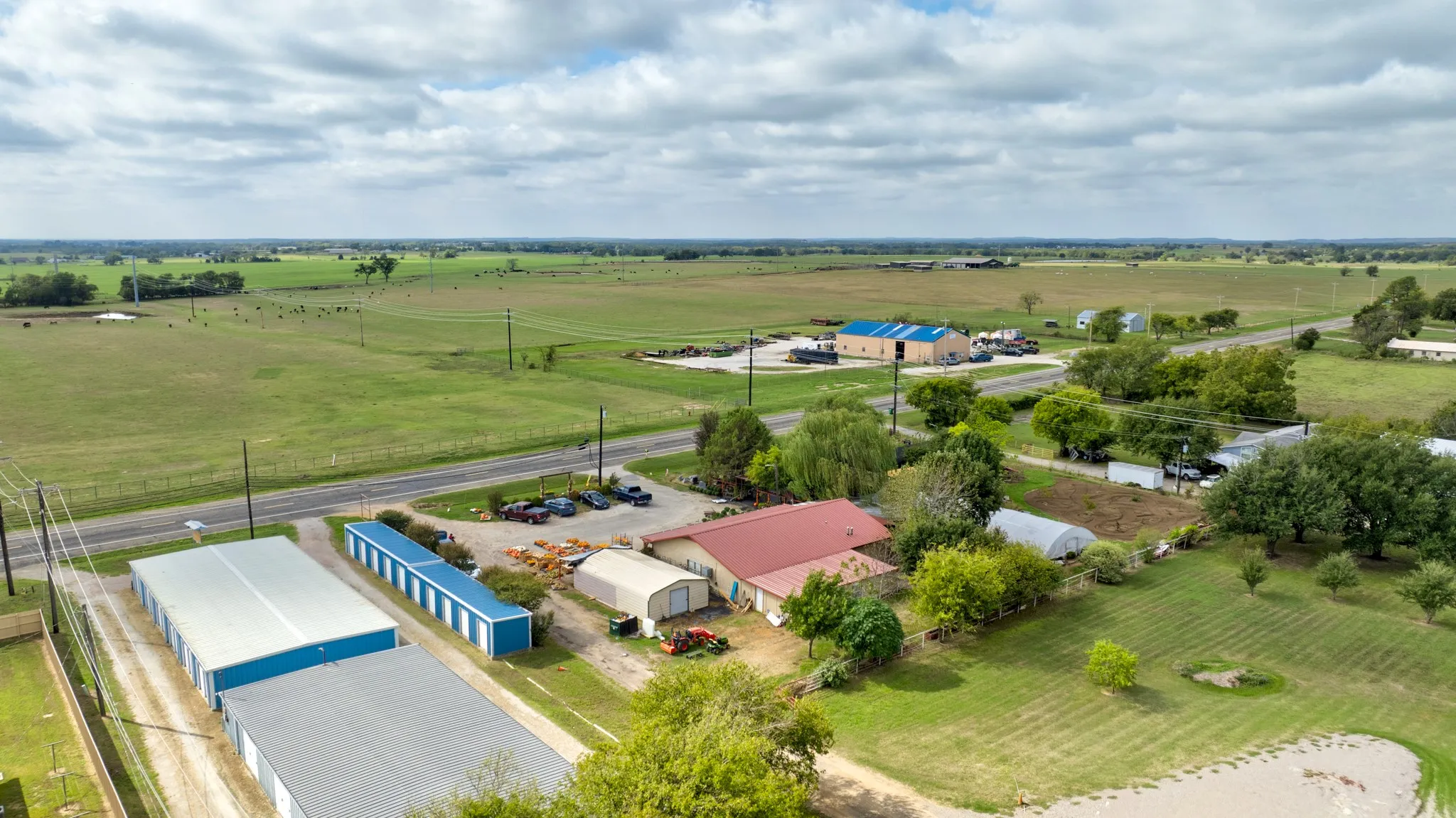 Expansive acreage featuring multiple metal-sided outbuildings, paved parking areas, gravel access drives, and mature trees
