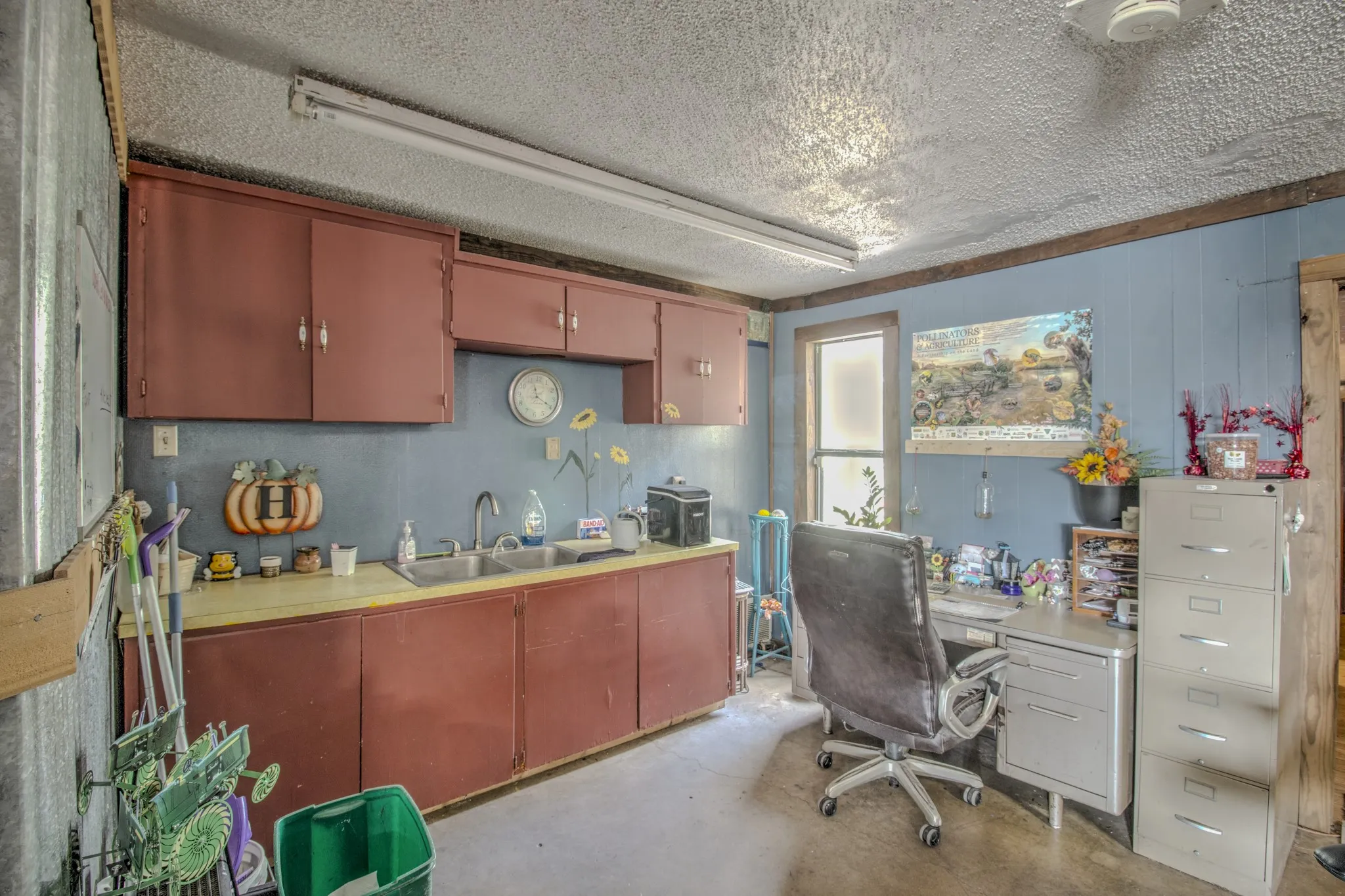 Utility area featuring wood cabinetry, a dual-basin stainless steel sink, a laminate countertop, and linear fluorescent lighting