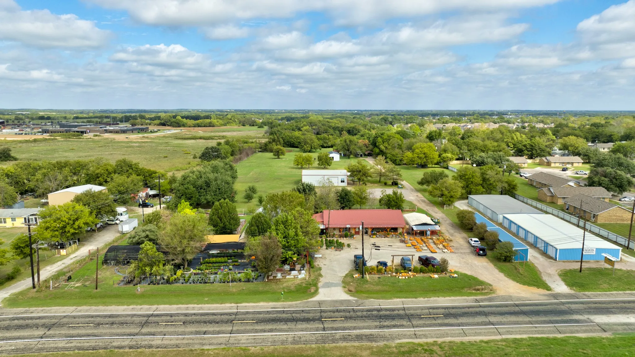 Aerial perspective featuring expansive acreage, a metal-roofed structure, secondary outbuildings, gravel access areas, and established perimeter landscaping