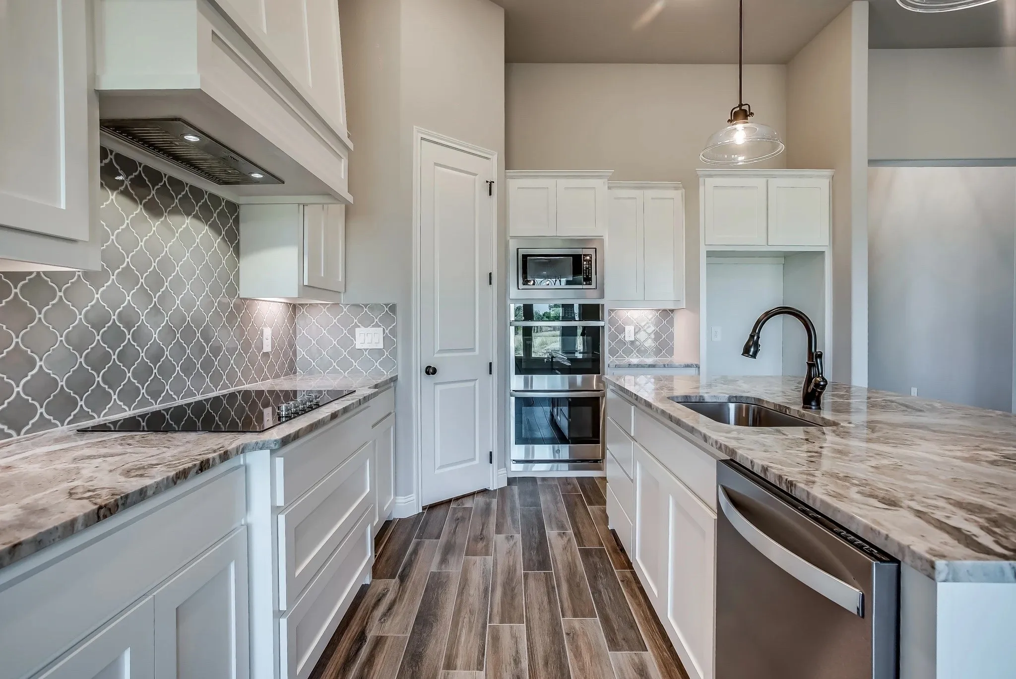 Kitchen featuring white shaker cabinetry, stone countertops, patterned tile backsplash, stainless steel double wall ovens, and wood-finish flooring