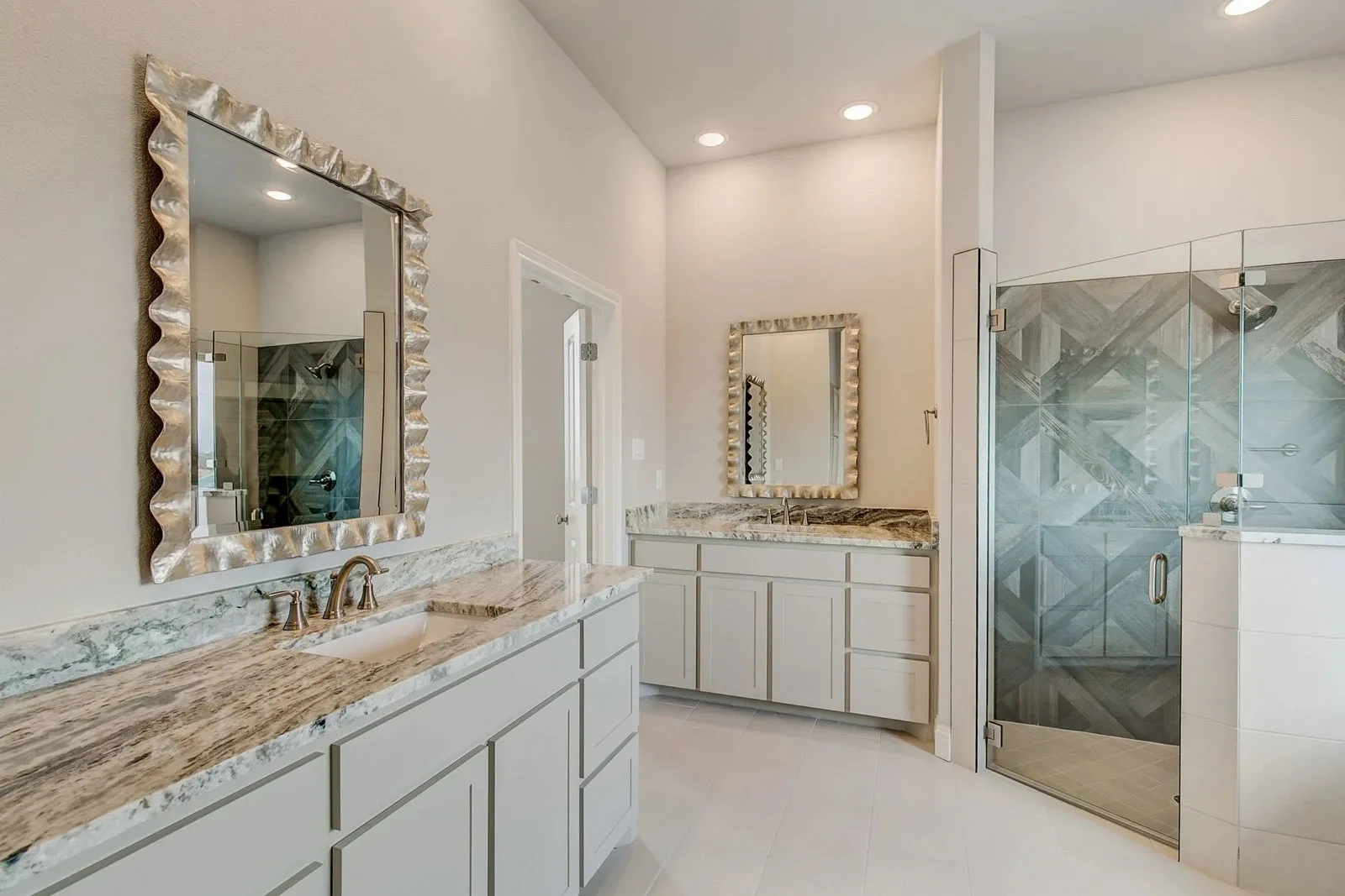 Dual vanity featuring stone countertops, undermount sinks, custom cabinetry, decorative mirrors, and a glass-enclosed shower with patterned wall tile