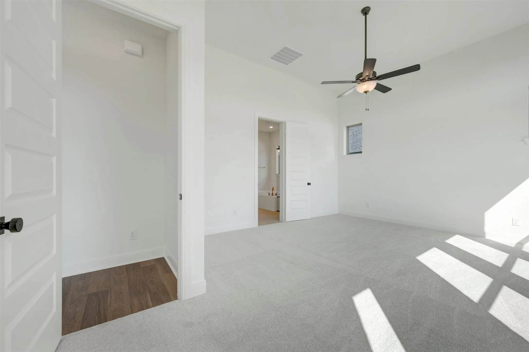 High-ceiling interior featuring carpeted flooring, a multi-paneled door, a dark-finish ceiling fan with integrated lighting, and a square window
