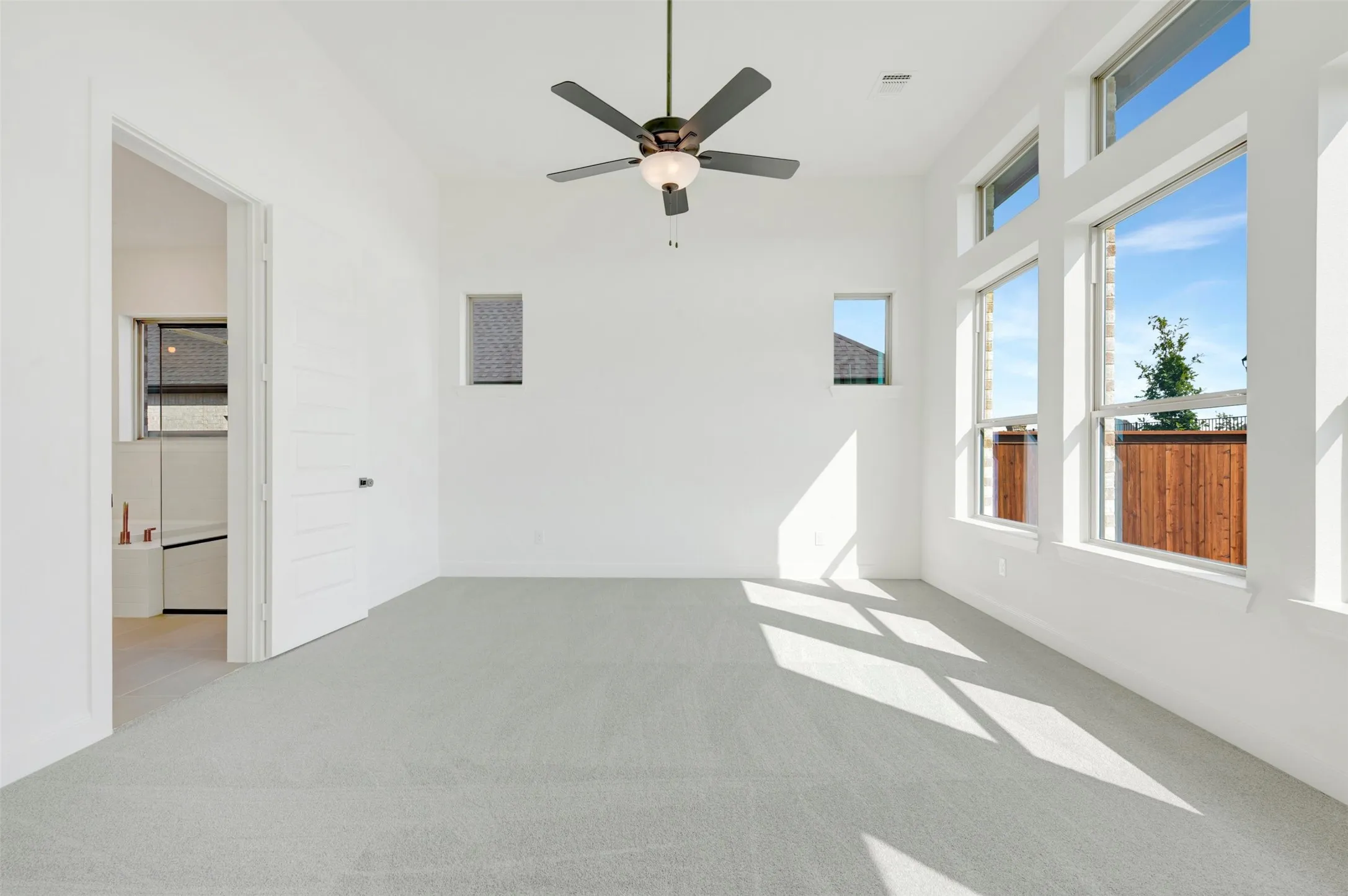 High-ceiling room featuring neutral carpeting, a central multi-blade ceiling fan with integrated lighting, oversized windows, and a multi-panel door