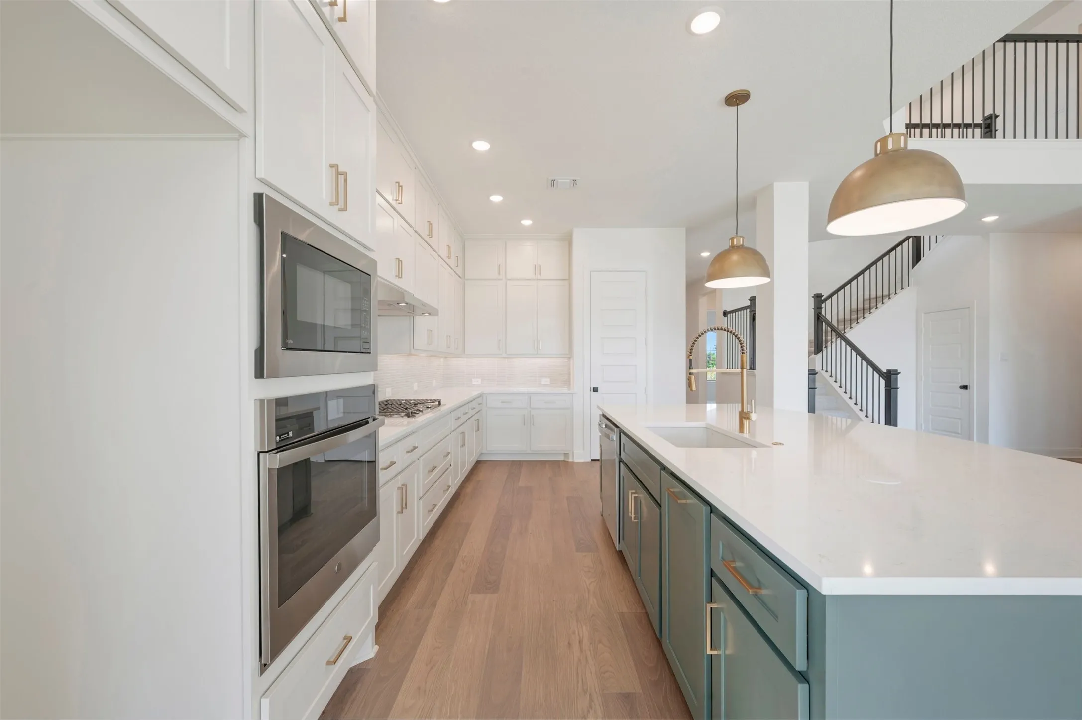 Kitchen featuring an oversized center island with stone-surface countertop, stainless steel double wall ovens, wood-finish flooring, and recessed lighting