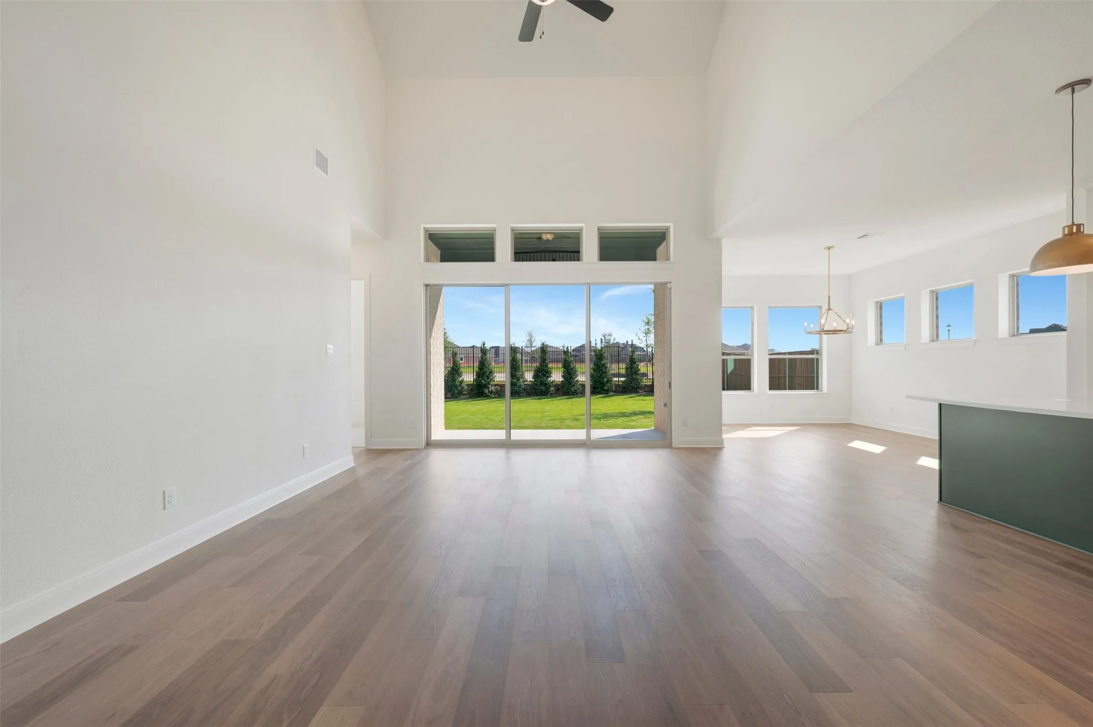 Vaulted ceilings, wood-finish flooring, expansive sliding glass doors, multiple pendant light fixtures, and a center island with a stone countertop