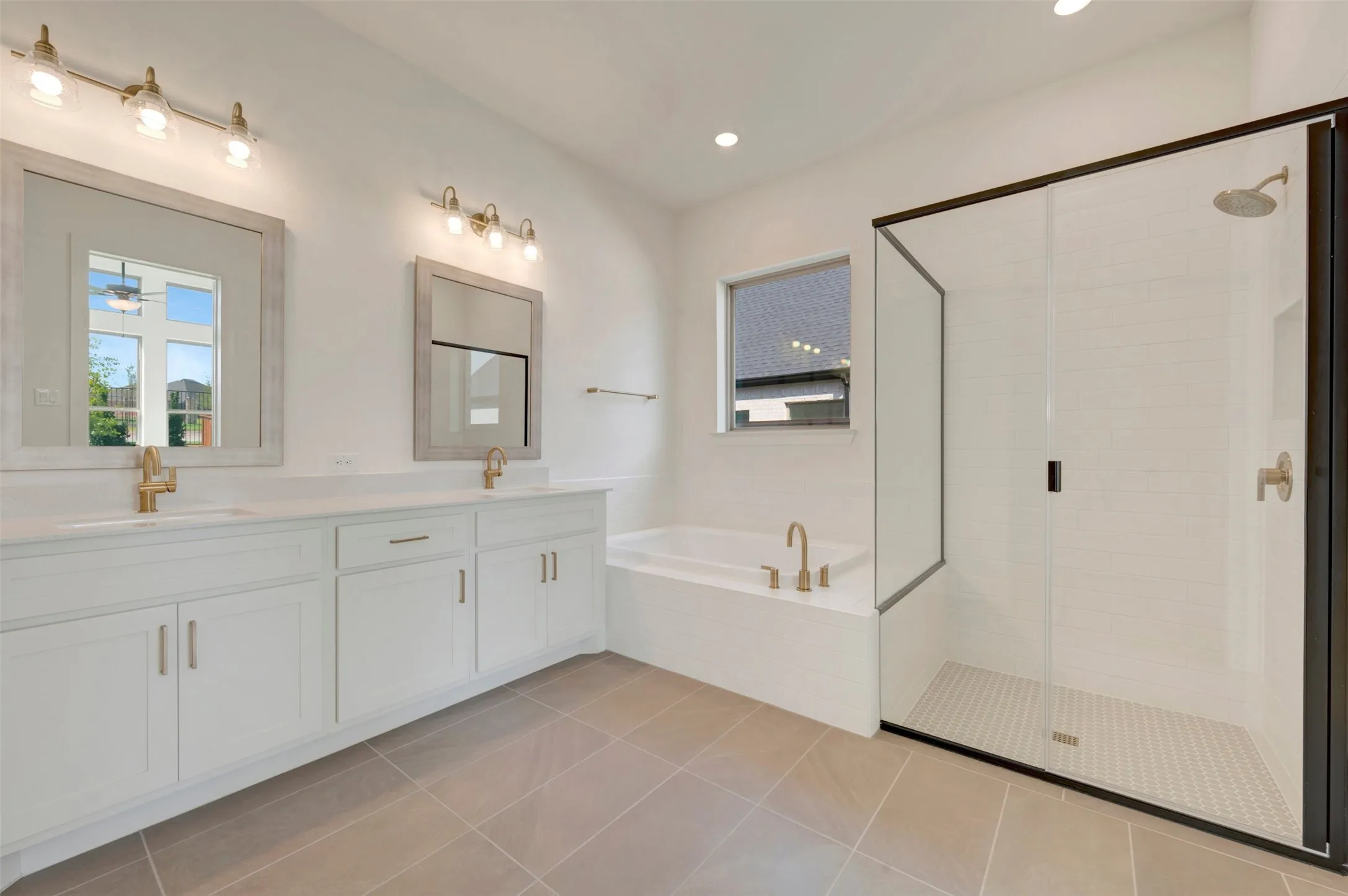 Bathroom featuring a double vanity with stone countertops, a tiled walk-in shower with a glass enclosure, a deep soaking tub, and brass-tone fixtures