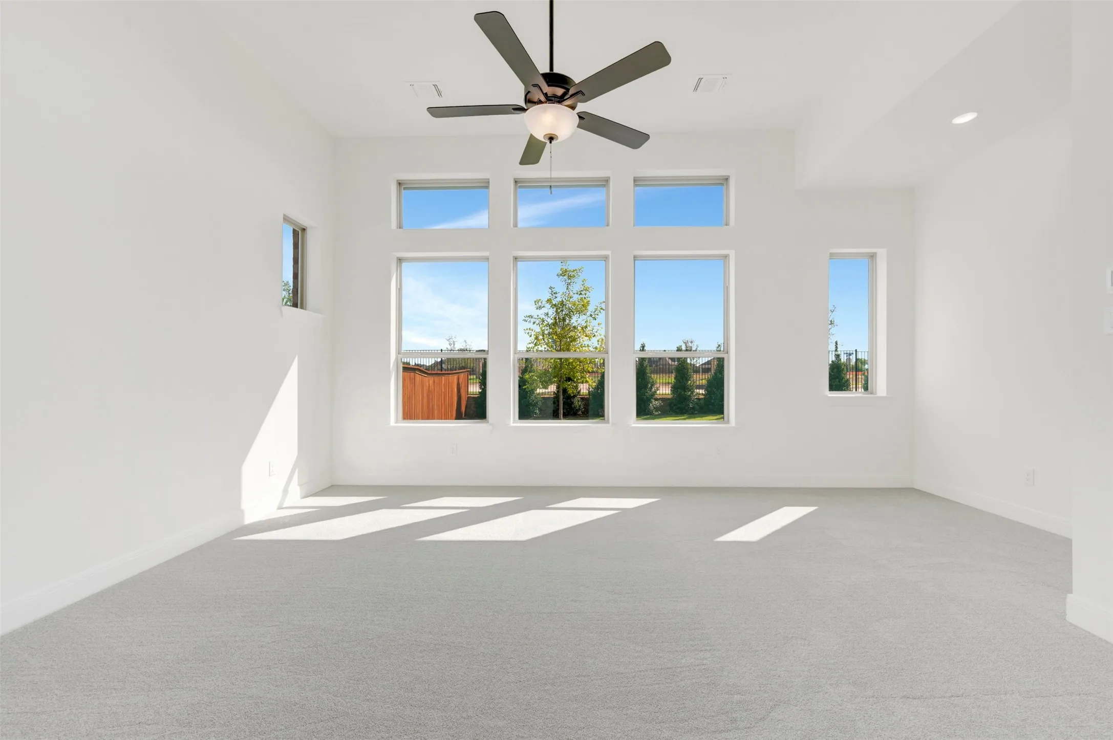 High ceilings with a central ceiling fan, neutral carpeting, and a series of large windows featuring natural light