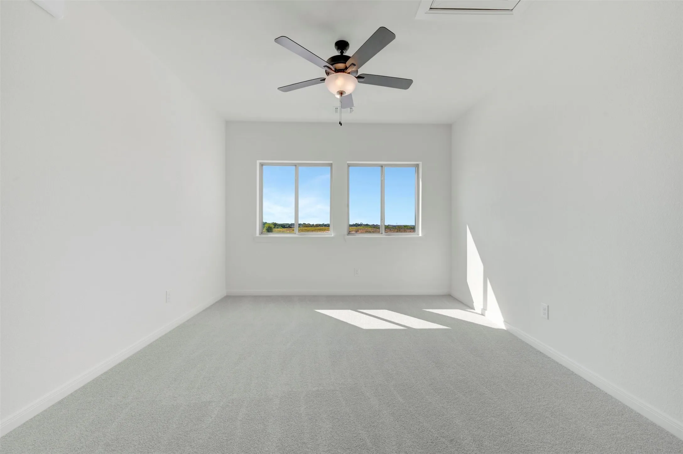 Interior room featuring wall-to-wall carpeting, dual windows, and a ceiling-mounted light fixture with a fan