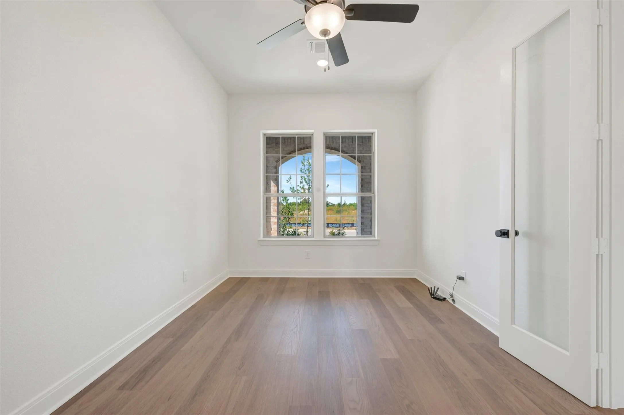 Wood-finish flooring, dual windows with arched brick surround, and a ceiling-mounted light fixture with fan