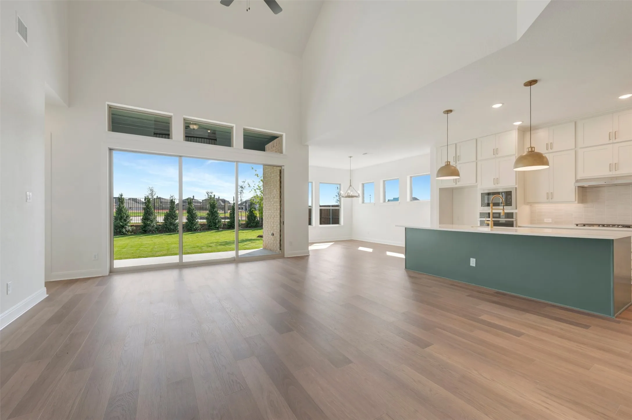 Vaulted ceilings with expansive floor-to-ceiling glass sliding doors, wood-finish flooring, kitchen island with quartz-surface countertop, and custom cabinetry with built-in stainless steel appliances