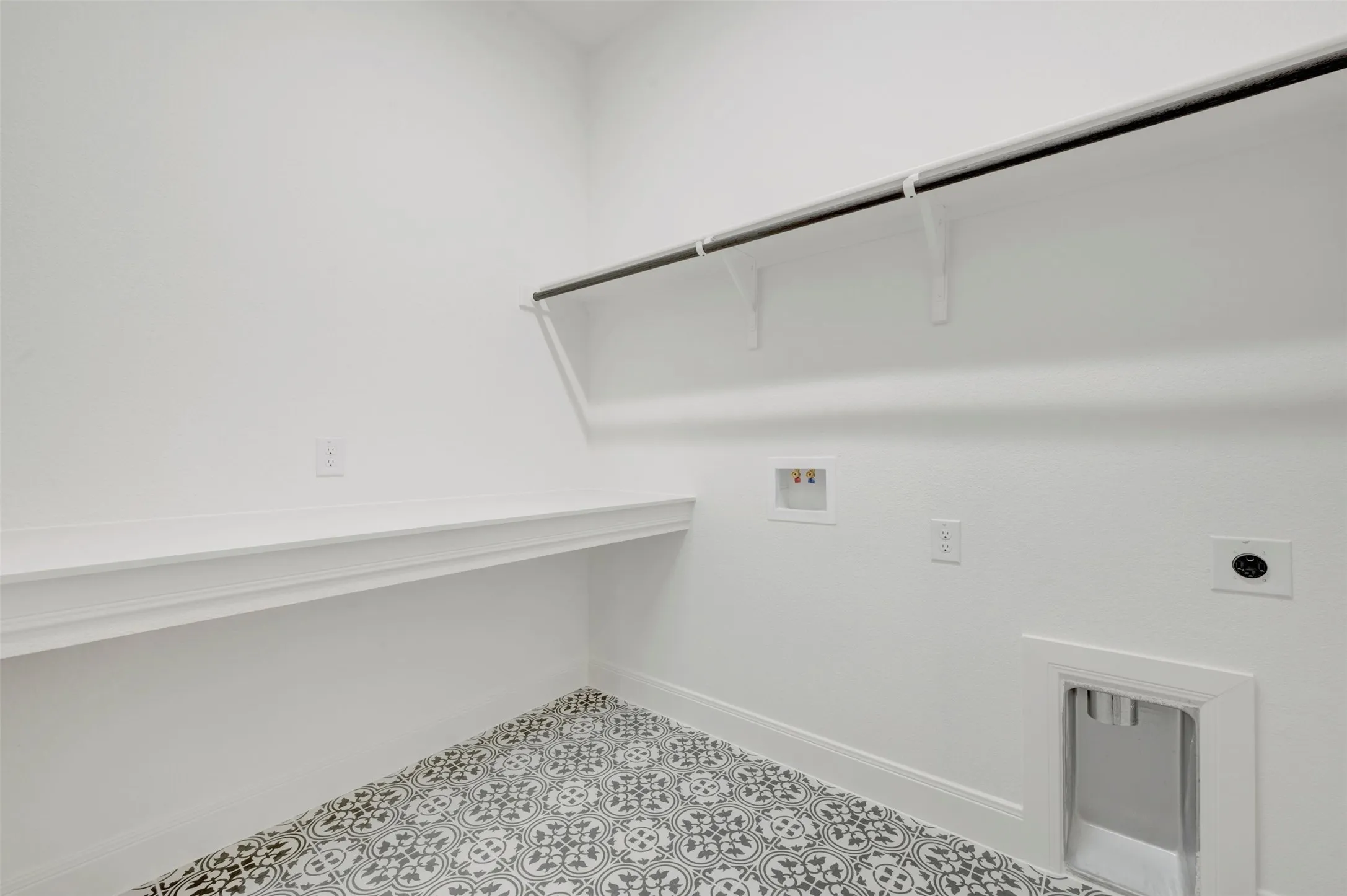 Laundry room featuring patterned tile flooring, built-in shelving, a wall-mounted hanging rod, and dedicated appliance hookups