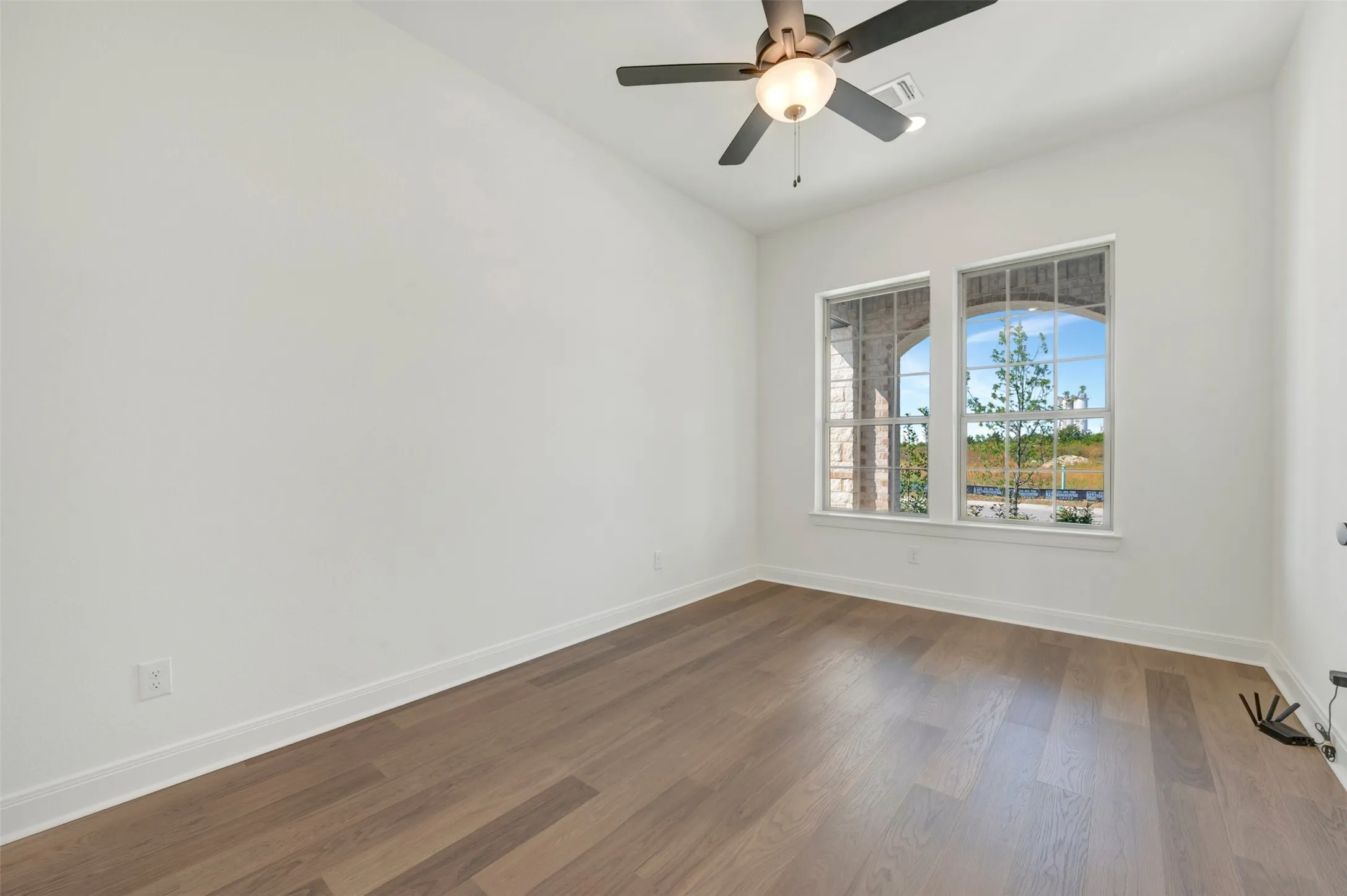 Wood-finish flooring, dual windows with arched masonry trim, and a ceiling-mounted fan with integrated lighting