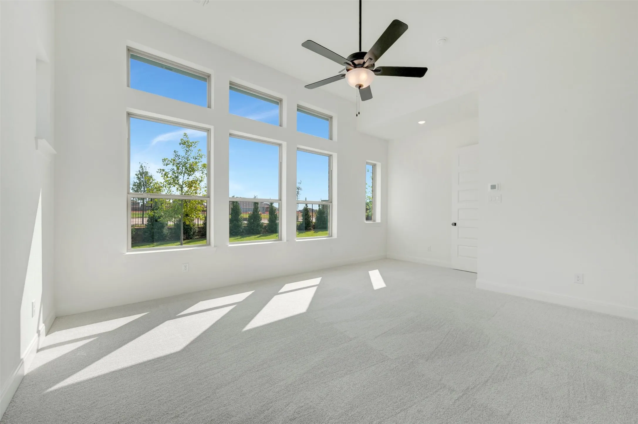 High ceilings featuring a matte black ceiling fan with an integrated light fixture, large paneled windows, and neutral carpeting