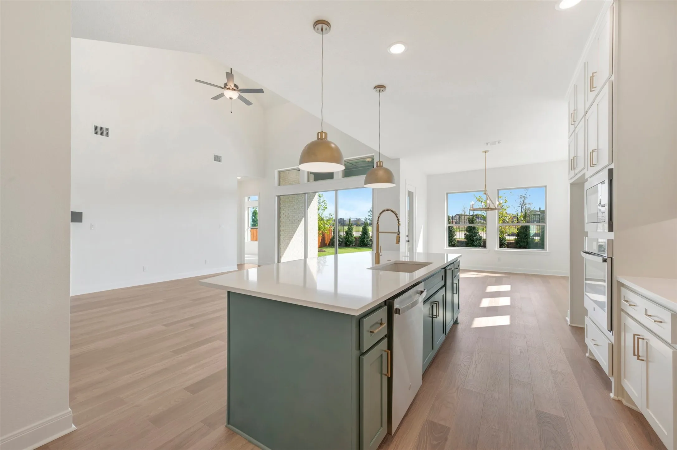 Kitchen featuring a central island with a quartz countertop, wood-finish flooring, vaulted ceilings, pendant lighting, and built-in wall oven cabinetry