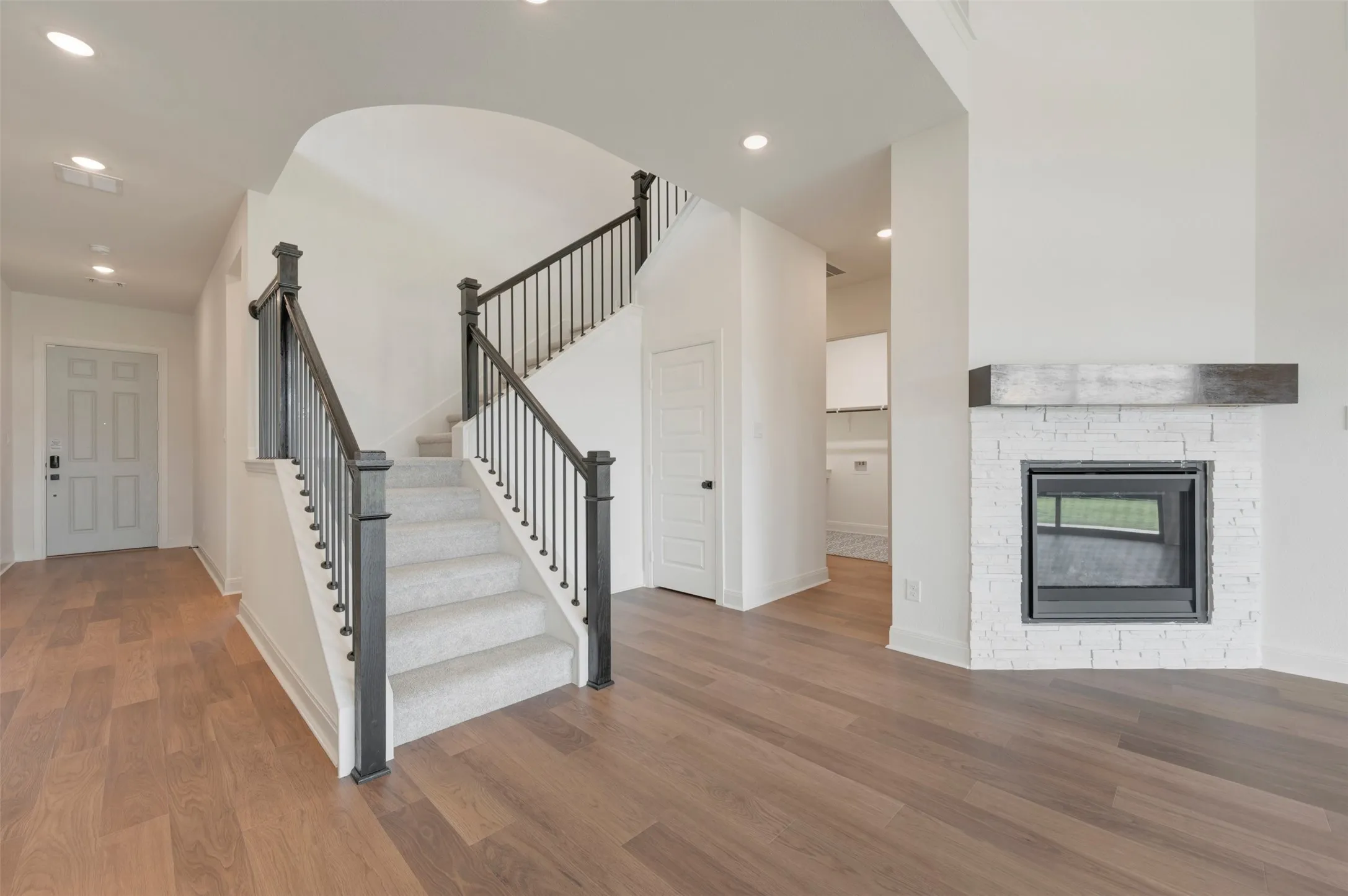Staircase with wooden handrails and balusters, wood-finish flooring, recessed lighting, and a white-painted brick fireplace featuring a dark wood mantel