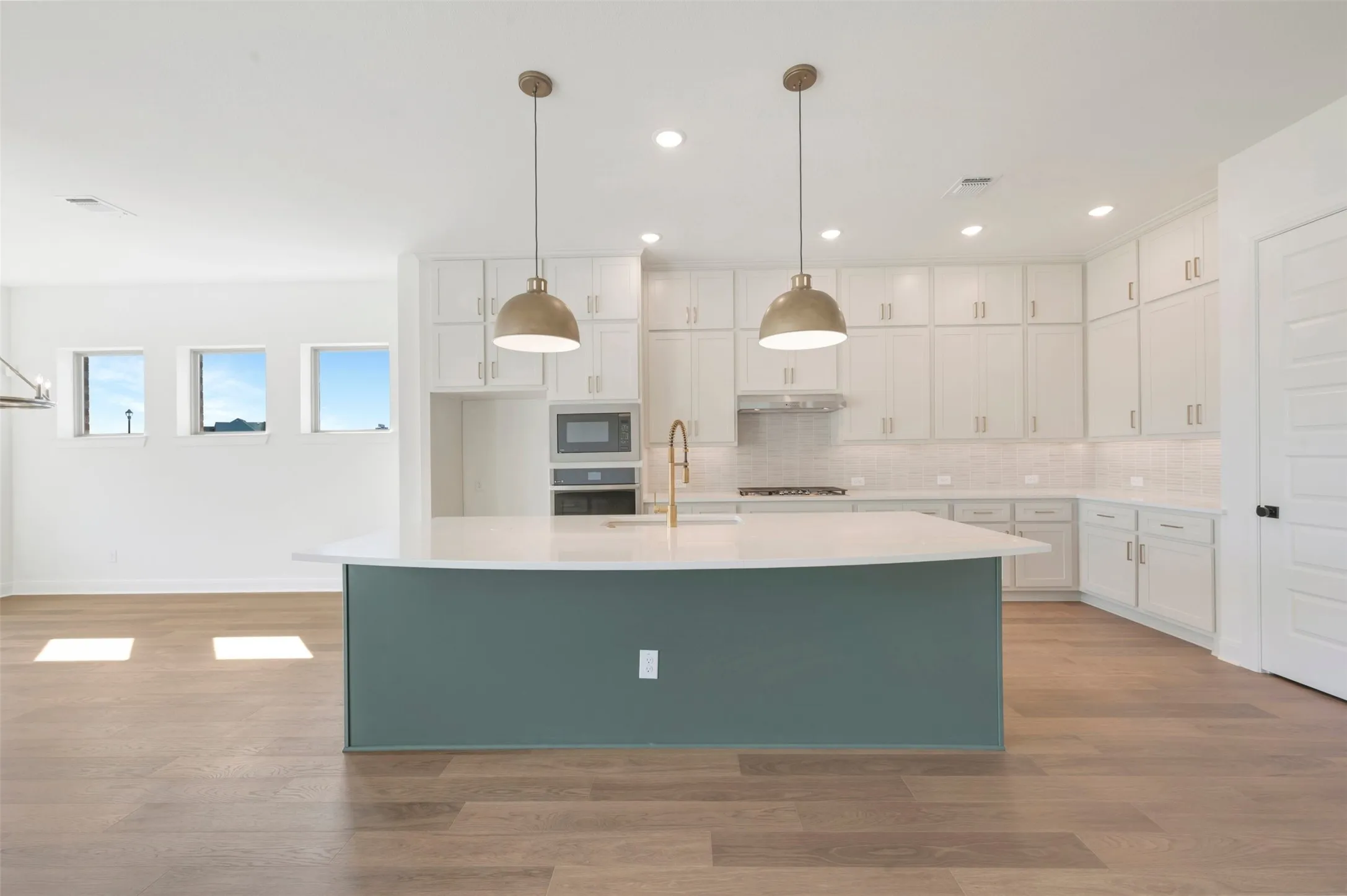 Kitchen featuring a center island with a solid surface countertop, white shaker-style cabinetry, wood-finish flooring, two metallic pendant lights, and a built-in wall oven and microwave