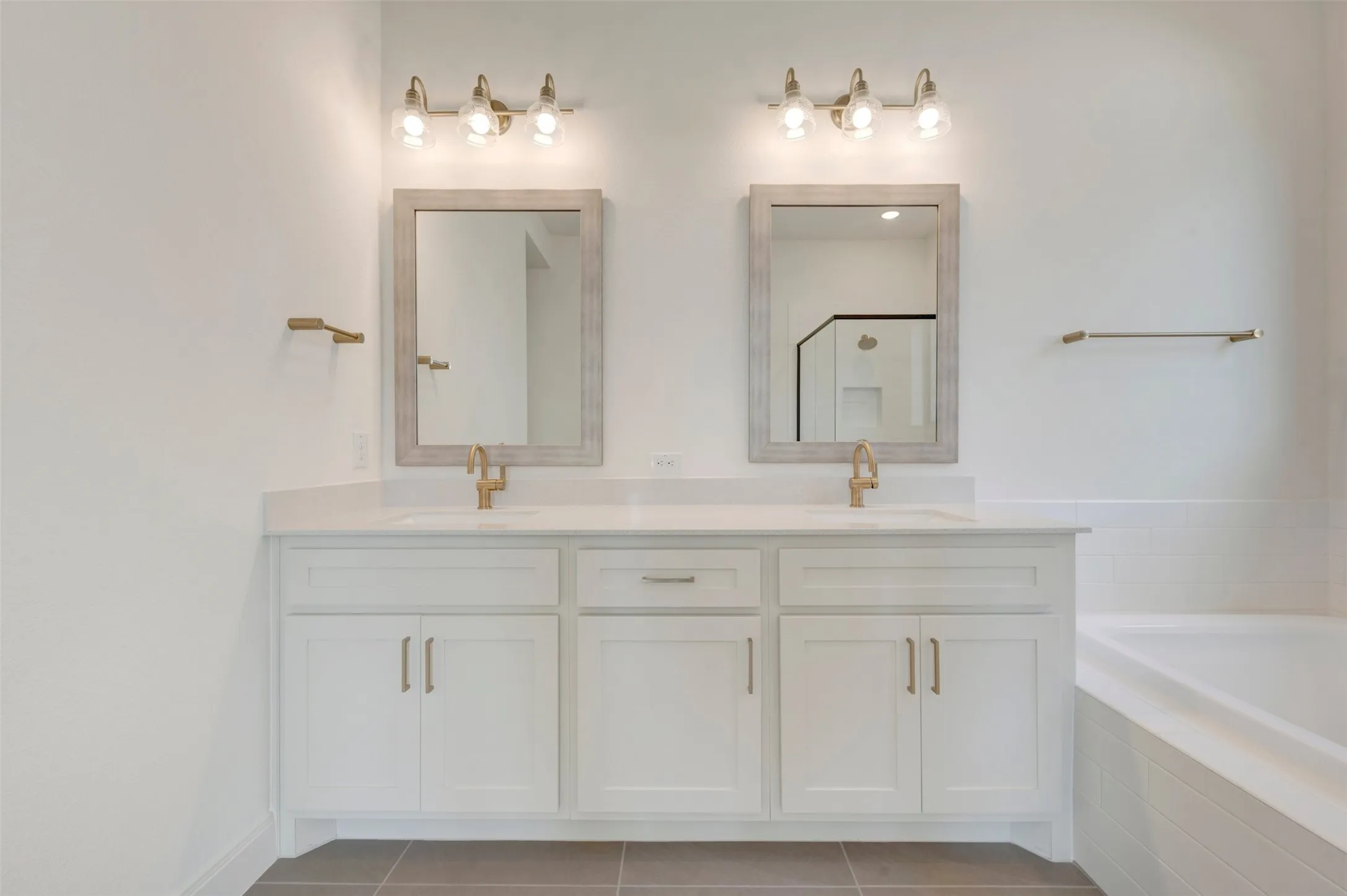 Double vanity featuring white cabinetry, a light-toned solid surface countertop, integrated dual sinks with metal fixtures, framed vanity mirrors, and three-light wall-mounted sconces