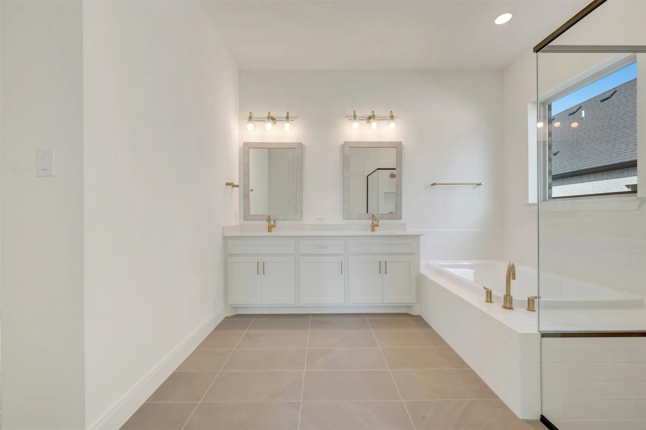 Double vanity with white cabinetry, rectangular drop-in sinks, brass-toned fixtures, wall-mounted rectangular mirrors, and a deep soaking tub