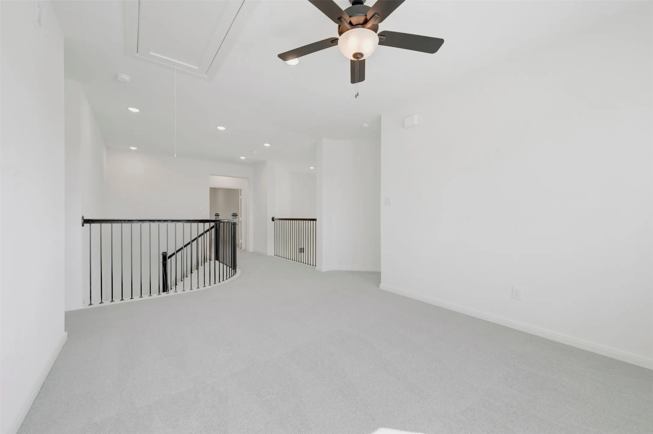 Open interior space featuring neutral carpeting, recessed lighting, a ceiling fan with integrated light fixture, and black metal spindle railing