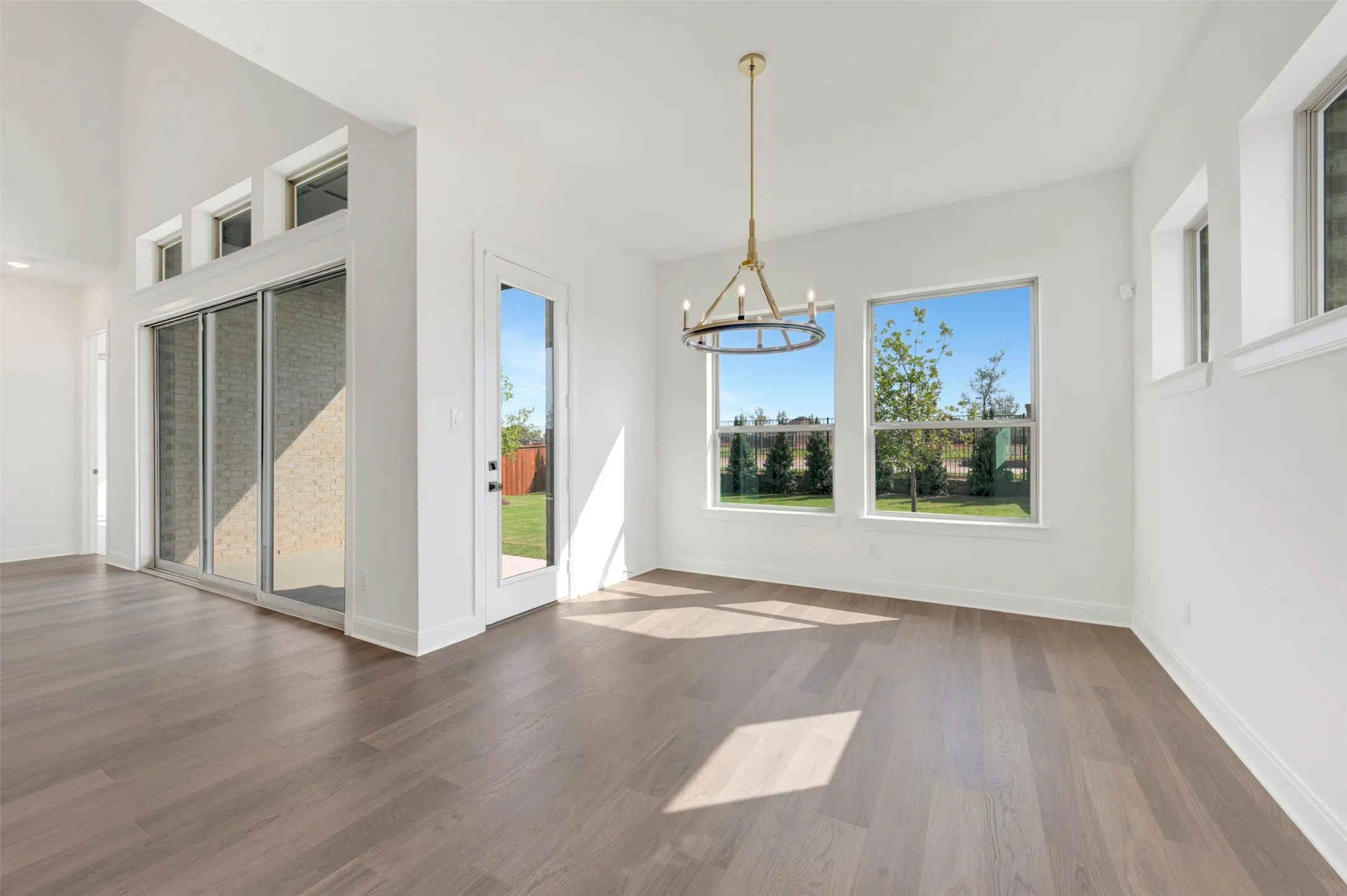 Vaulted ceilings, wood-finish flooring, sliding glass door, multi-light metal chandelier, and large windows
