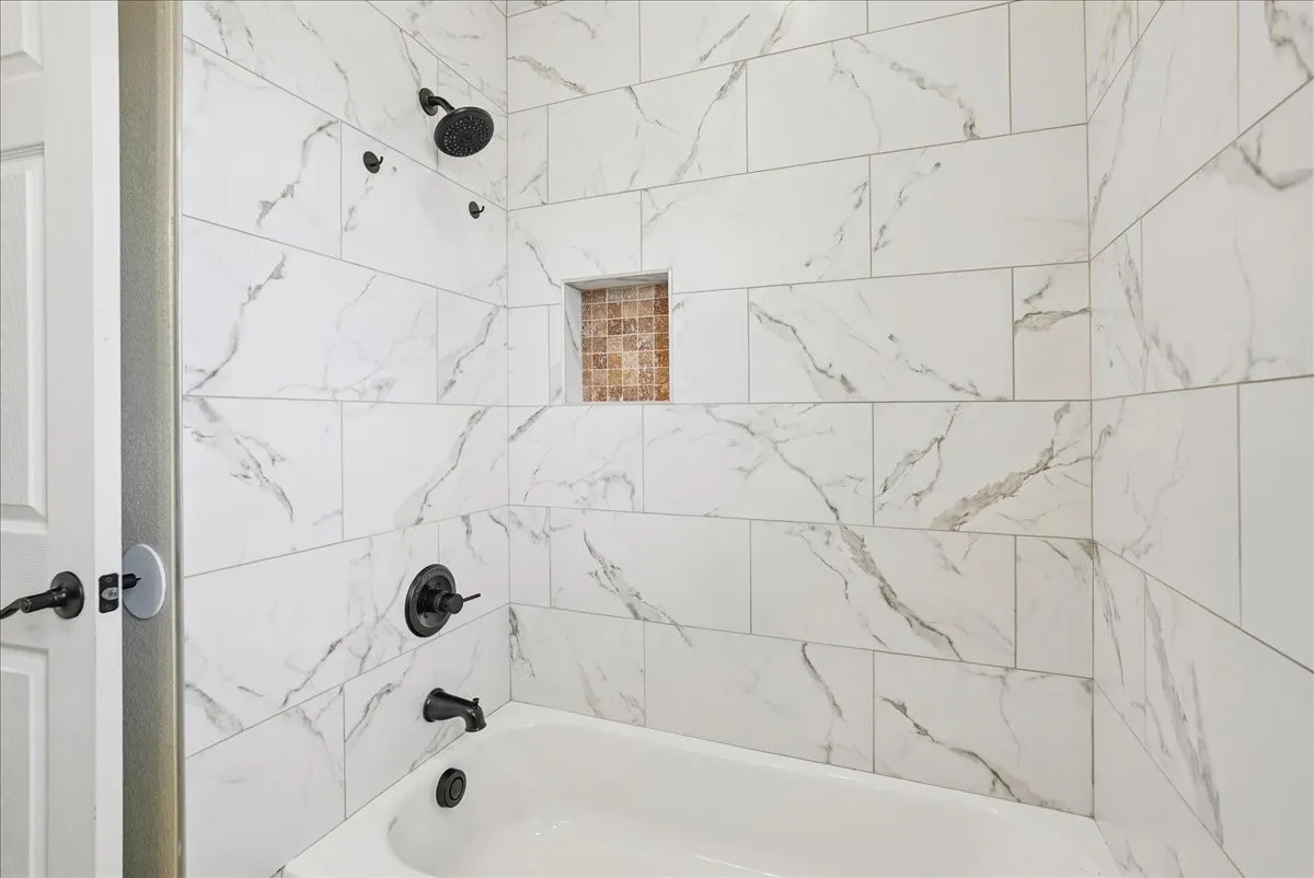 Shower enclosure featuring large-format veined tile surround, recessed mosaic niche, matte black fixtures, and a white soaking tub