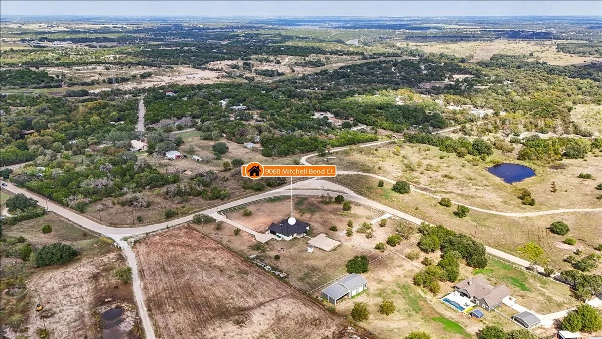 Aerial perspective featuring expansive acreage, a circular driveway, a detached outbuilding, and mature trees on the property grounds