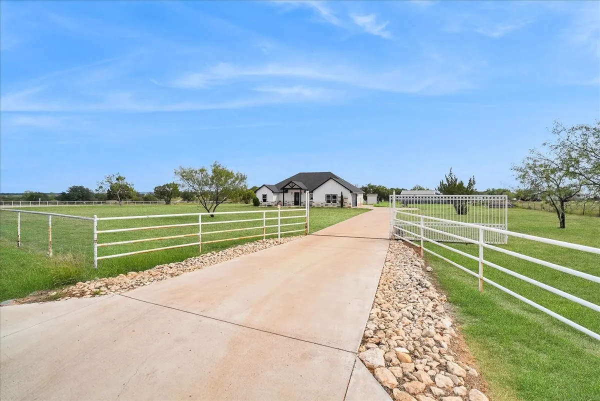 Concrete driveway with gravel bordering, expansive fenced acreage, and gated entrance