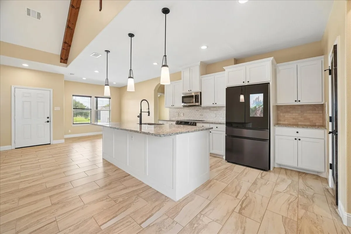 Kitchen featuring an expansive center island with a stone-finish countertop, white shaker-style cabinetry, a vaulted ceiling with exposed wood beam detail, and large-format tile flooring