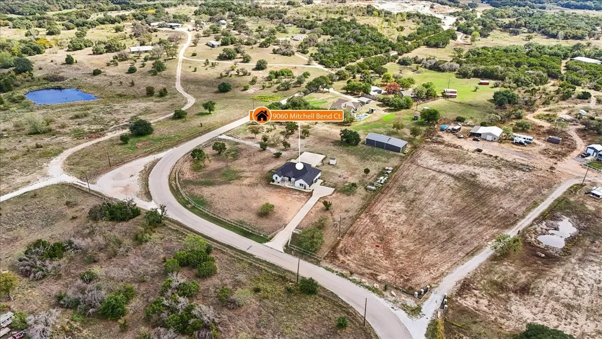 Aerial perspective of a detached residence featuring a paved driveway, expansive acreage, and native landscape