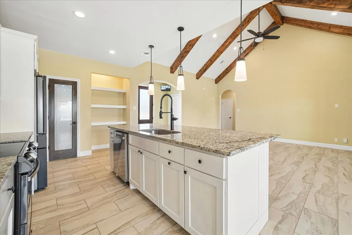 Vaulted ceiling with exposed wood beams, kitchen island with stone countertop, tile flooring, pendant lighting, and built-in shelving