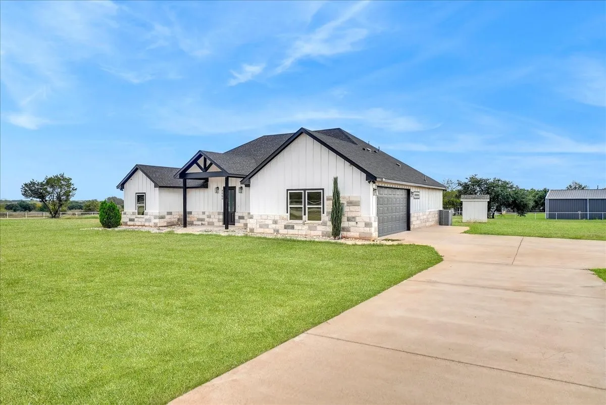 Exterior featuring board and batten siding, stone masonry wainscoting, a covered front entry, and a concrete driveway