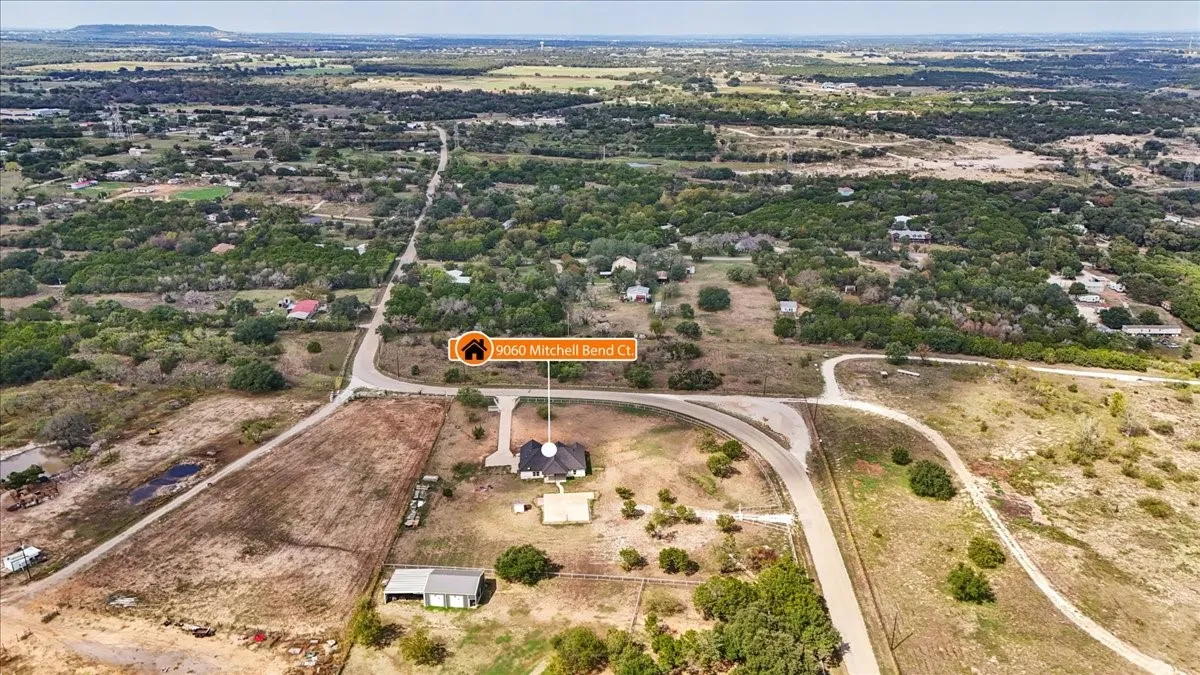 Aerial perspective of a sprawling acreage lot featuring a residential structure, detached workshop, paved driveway, and established native vegetation