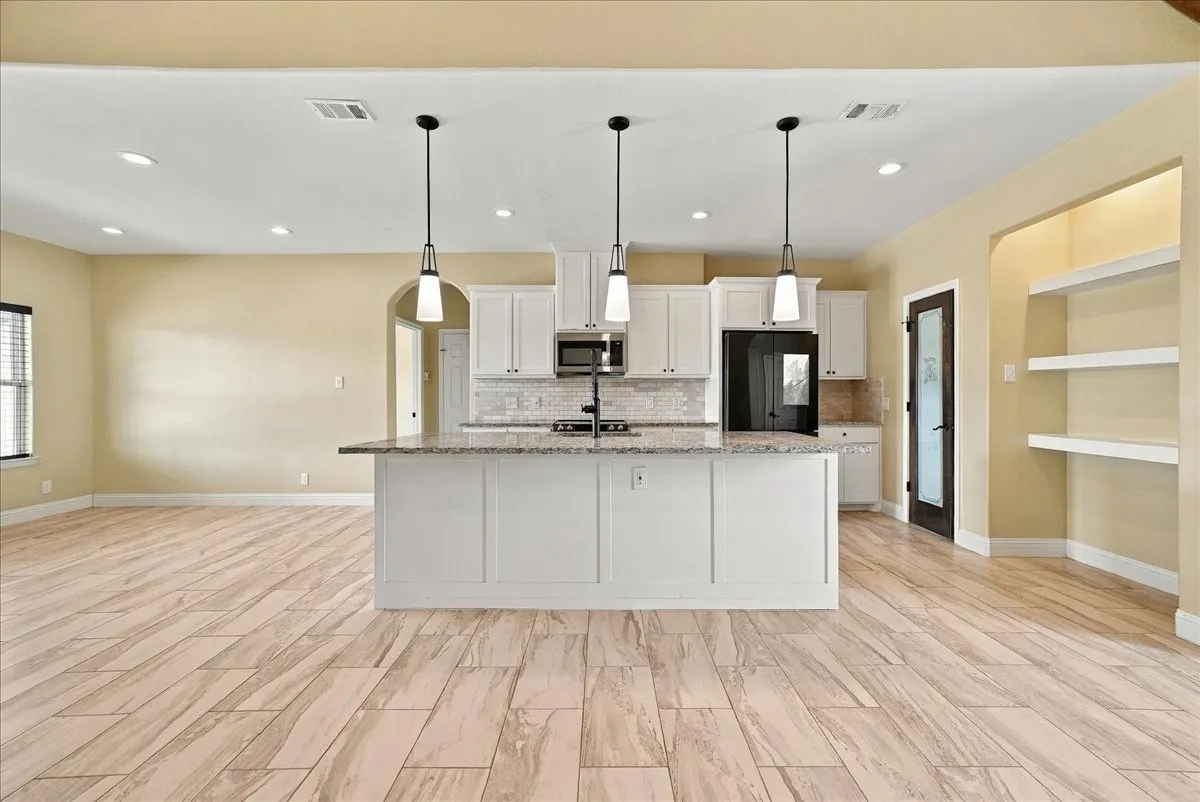 Kitchen featuring a central island with stone countertop, white cabinetry, recessed lighting, trio of pendant lights, and wood-finish flooring